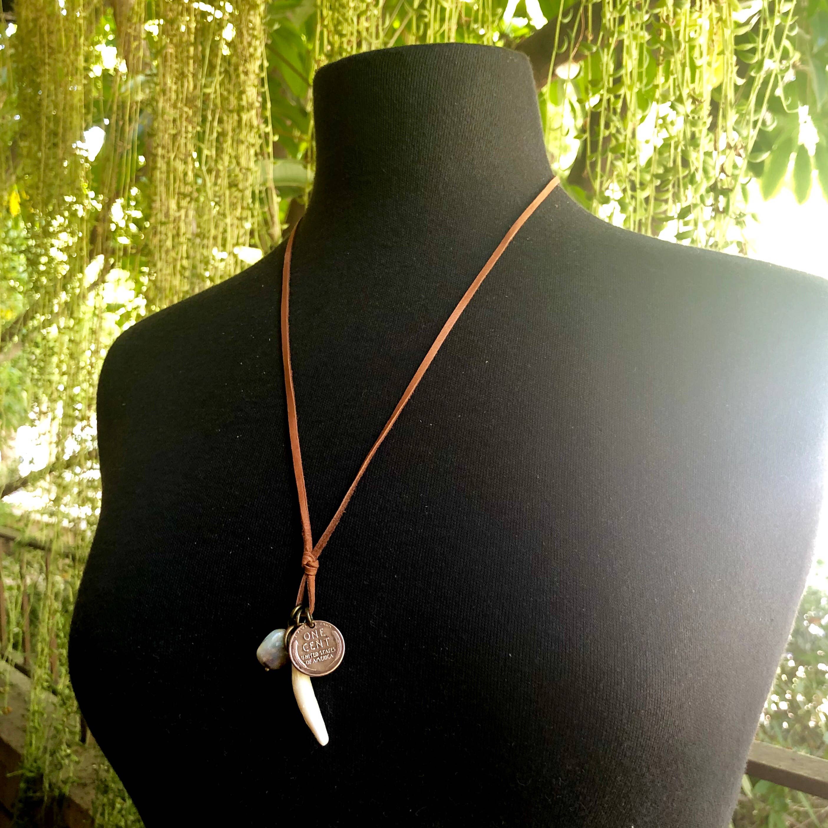 Coyote Tooth & Blue Opal Necklace, Wheat Penny, Rust Leather displayed on black mannequin against natural greenery background