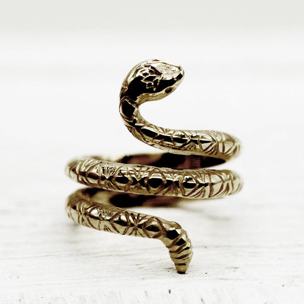 The Rattlesnake Lotus Ring by bahgsu jewels features a coiled snake design with detailed scales. This handcrafted brass minimalist statement ring is shown upright on a white wooden surface.