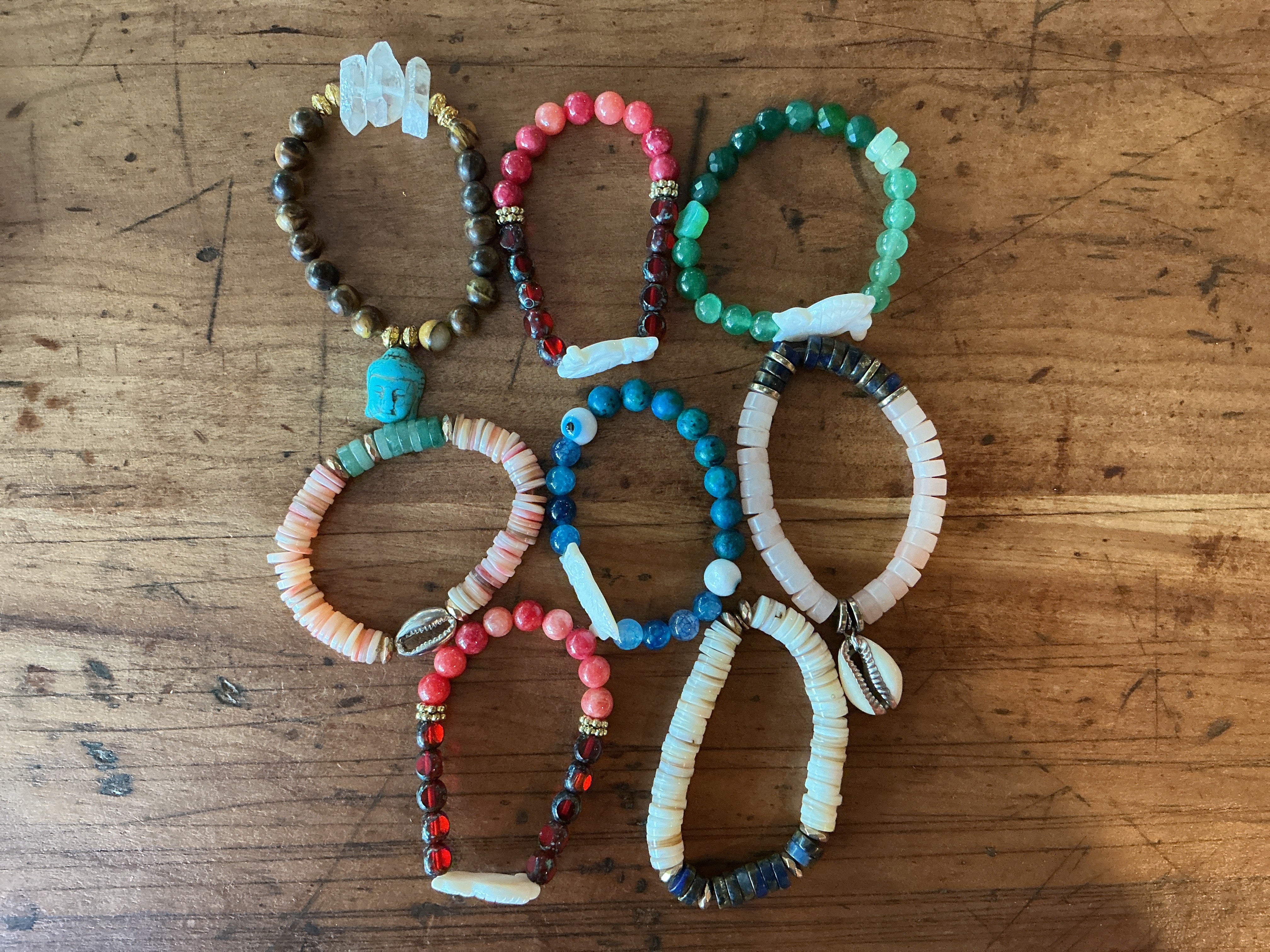 Beaded bracelet collection featuring colorful glass and shell beads with artisanal, boho-inspired styling on wood surface