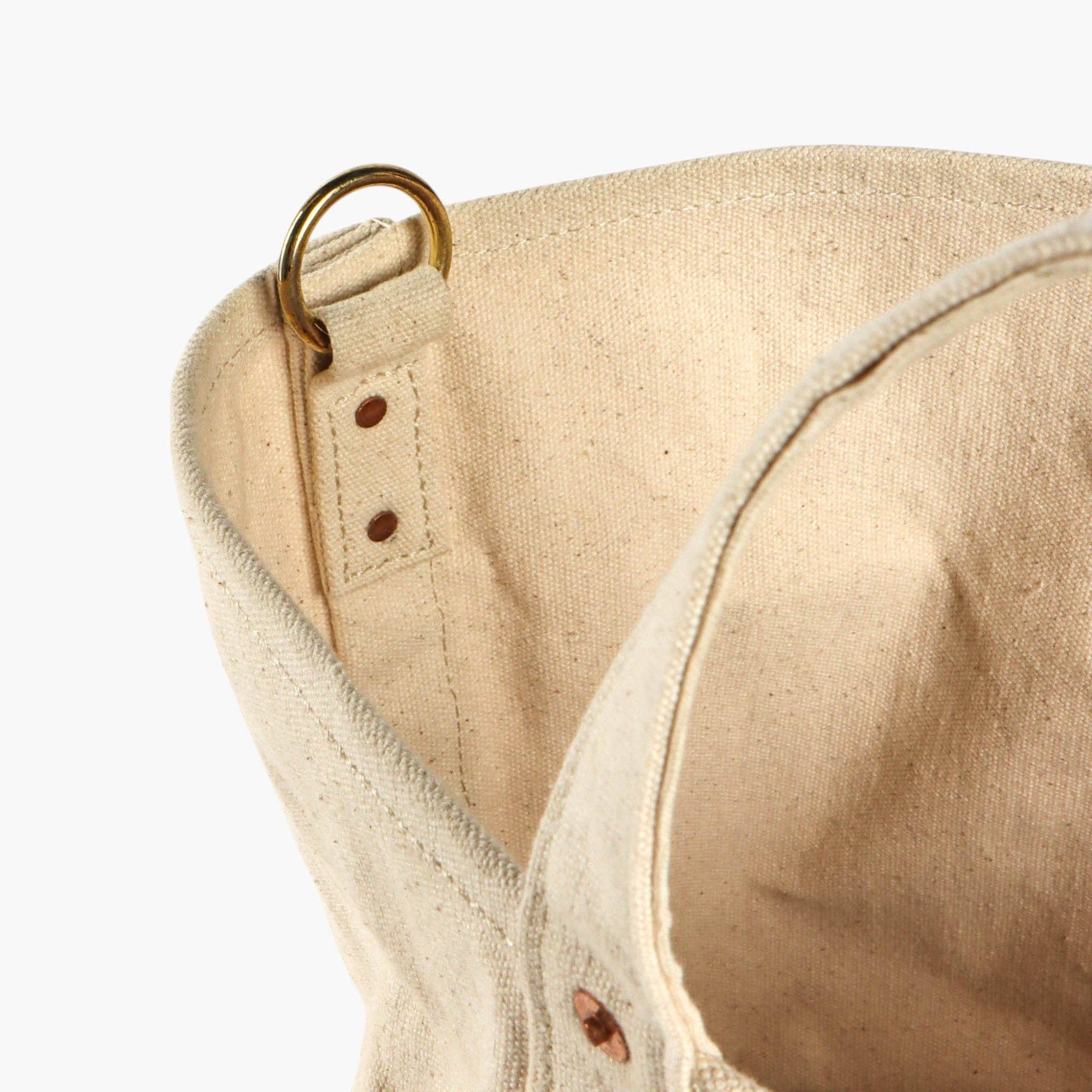 Close-up of undyed canvas Electrician Tote Strap with brass ring and reinforced stitching detail