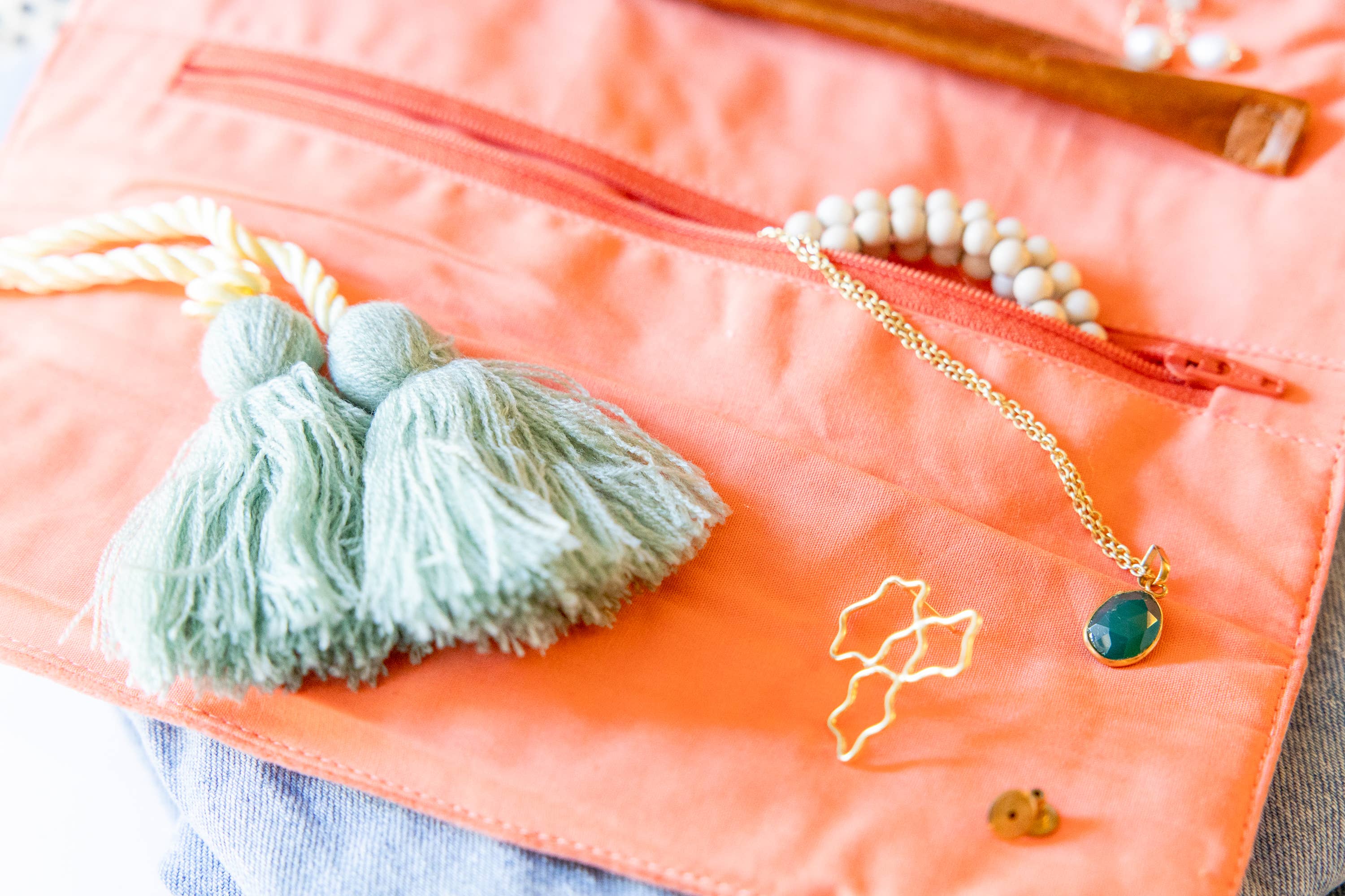 Embroidered Velvet Jewelry Organizer-Coral with soft tassels, gold necklace, and beaded bracelet on light fabric background
