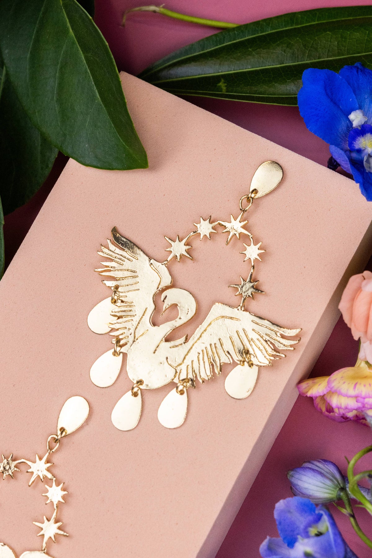 Celestial Swans gold swan statement earrings with star accents on a pink display card