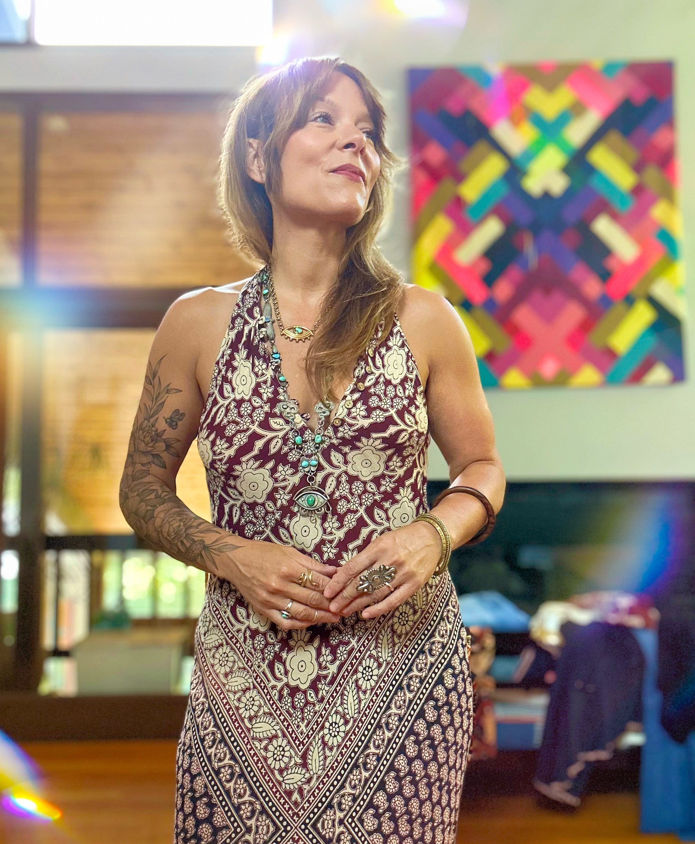 Woman in a patterned dress standing in a room with colorful abstract art on the wall.