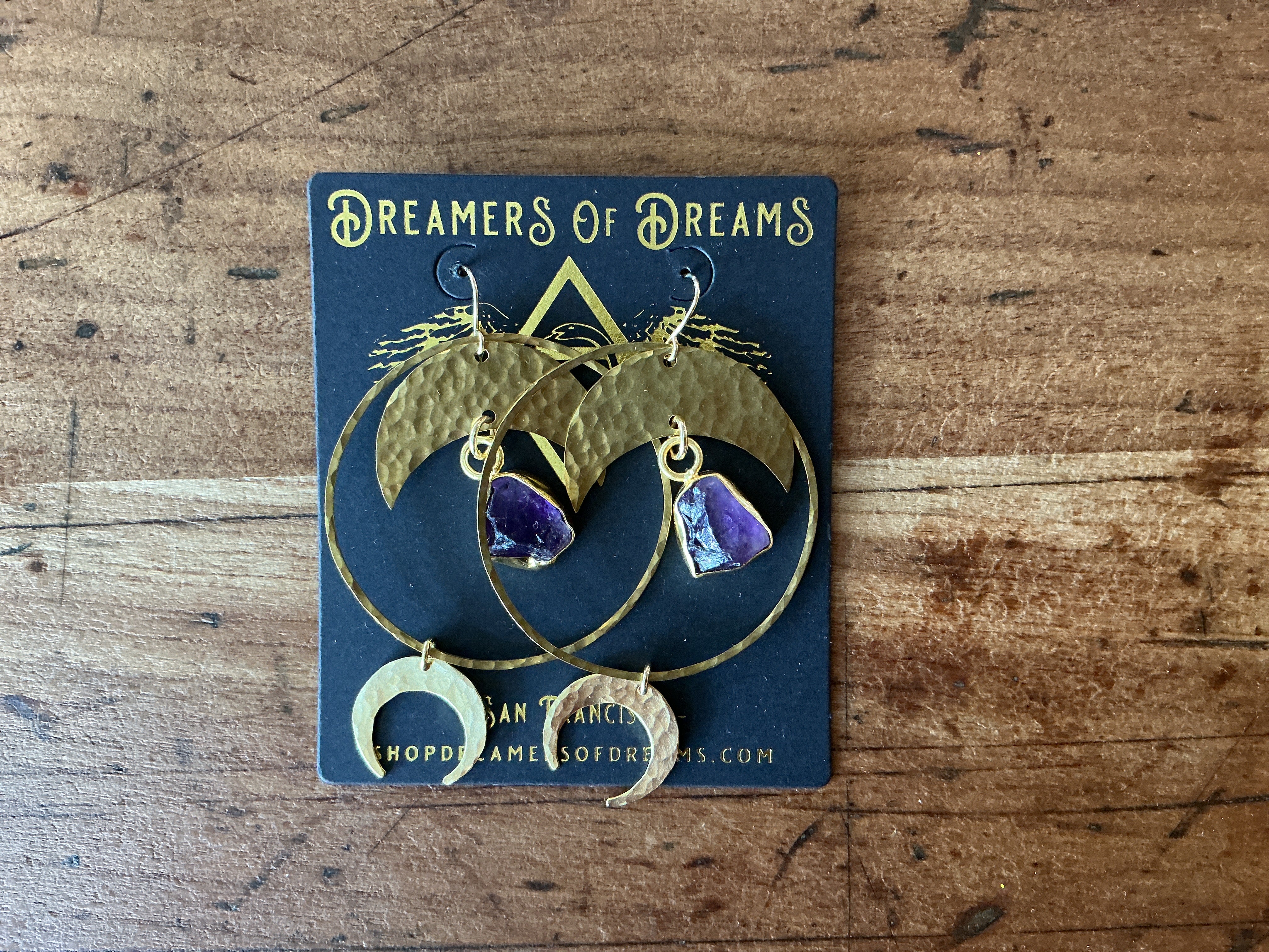 Halo Moon Hoops featuring hammered brass crescent shapes with purple stone accents on a rustic wooden surface
