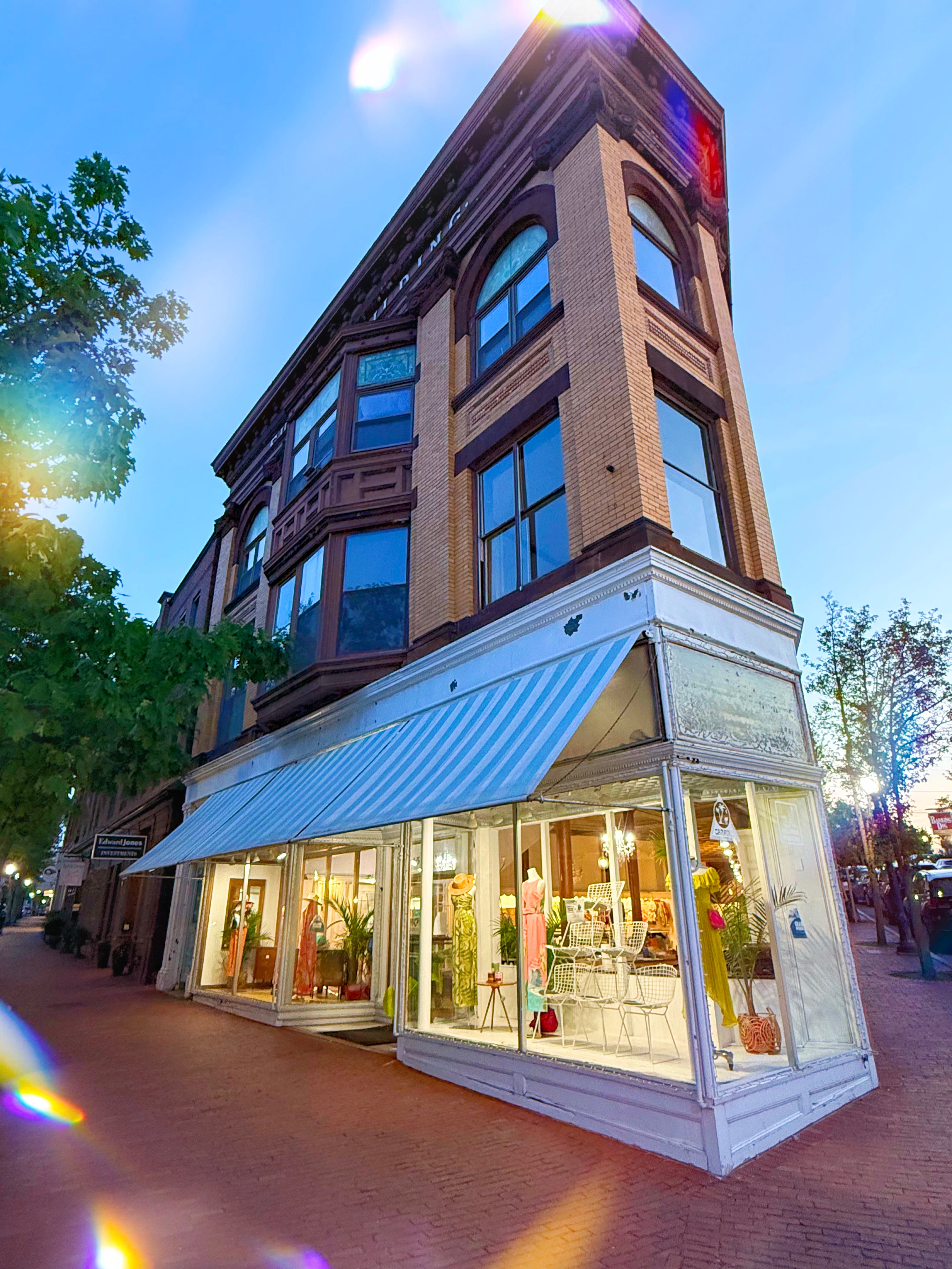 Tall brick building with large windows and a white awning on a street corner.