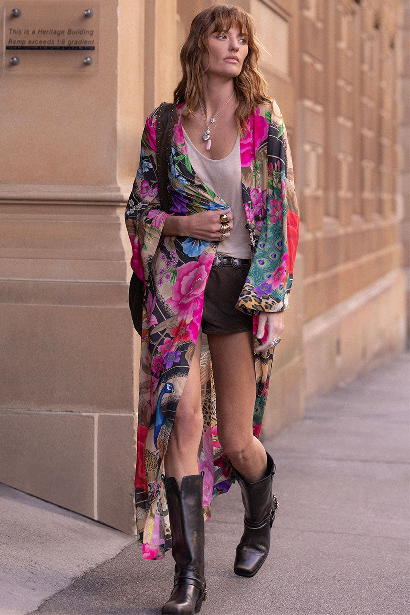 Woman wearing a colorful floral Valley of the Dolls Duster layered over casual shorts and boots on city street.