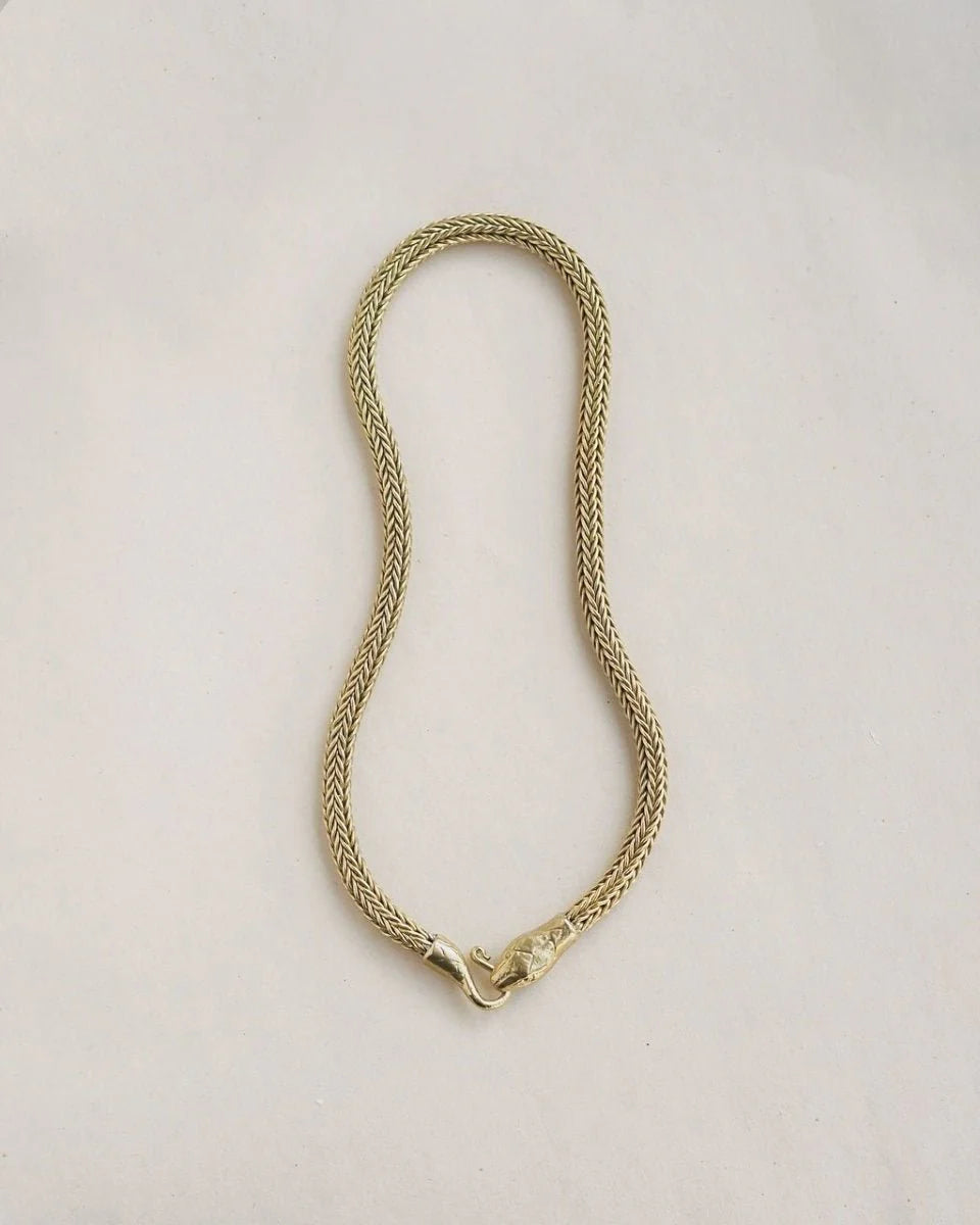 Serpent Choker Necklace in brass with woven chain and detailed snakehead clasp on neutral background