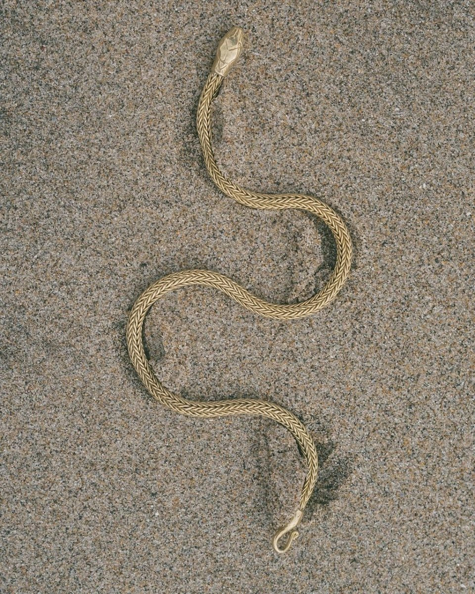 Serpent Choker Necklace in gold-tone with intricate braided design, shaped like a snake on sandy background
