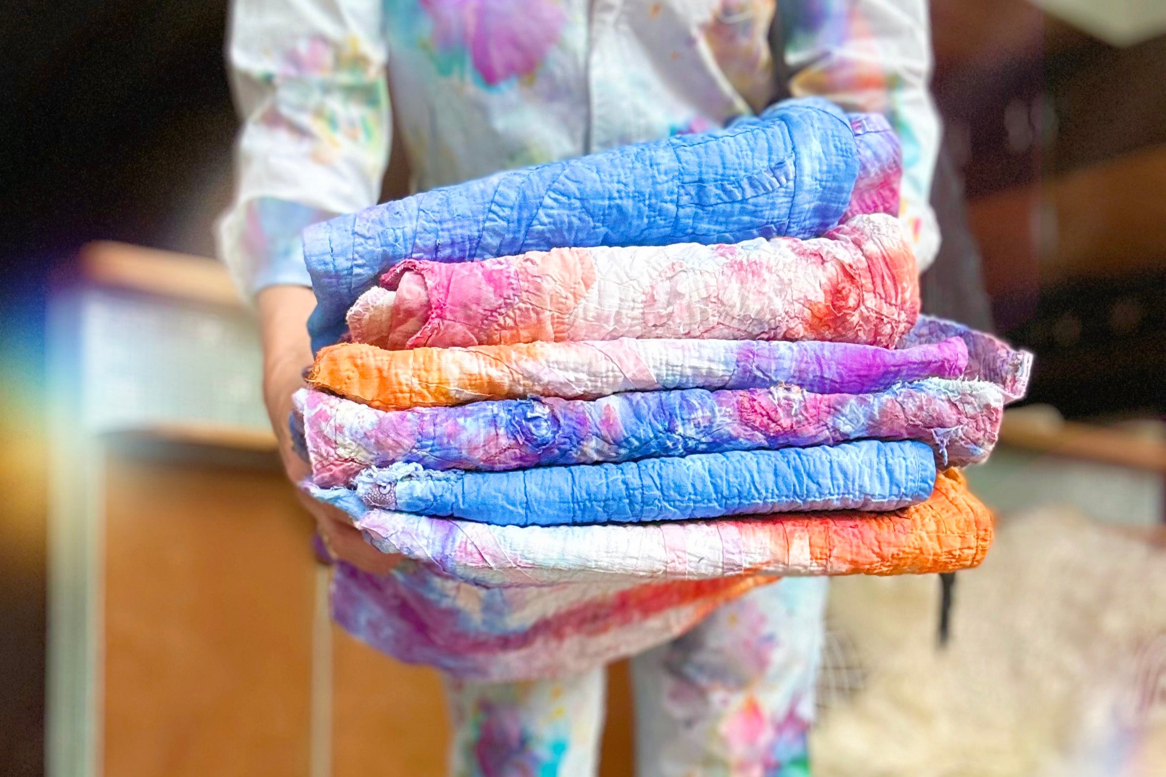 Person holding a stack of colorful folded blankets indoors.