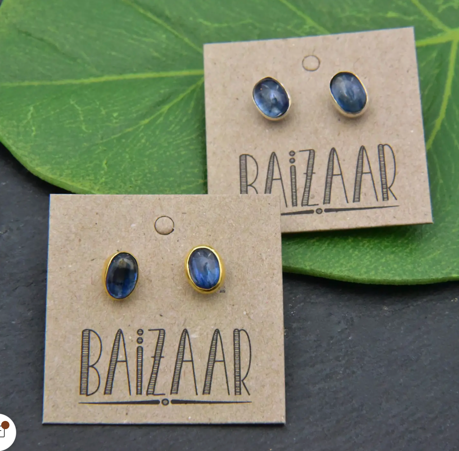 Two pairs of Caravan Sterling Silver Tanzanite Stud Earrings are shown on brown cards, resting on a green leaf and a dark surface.