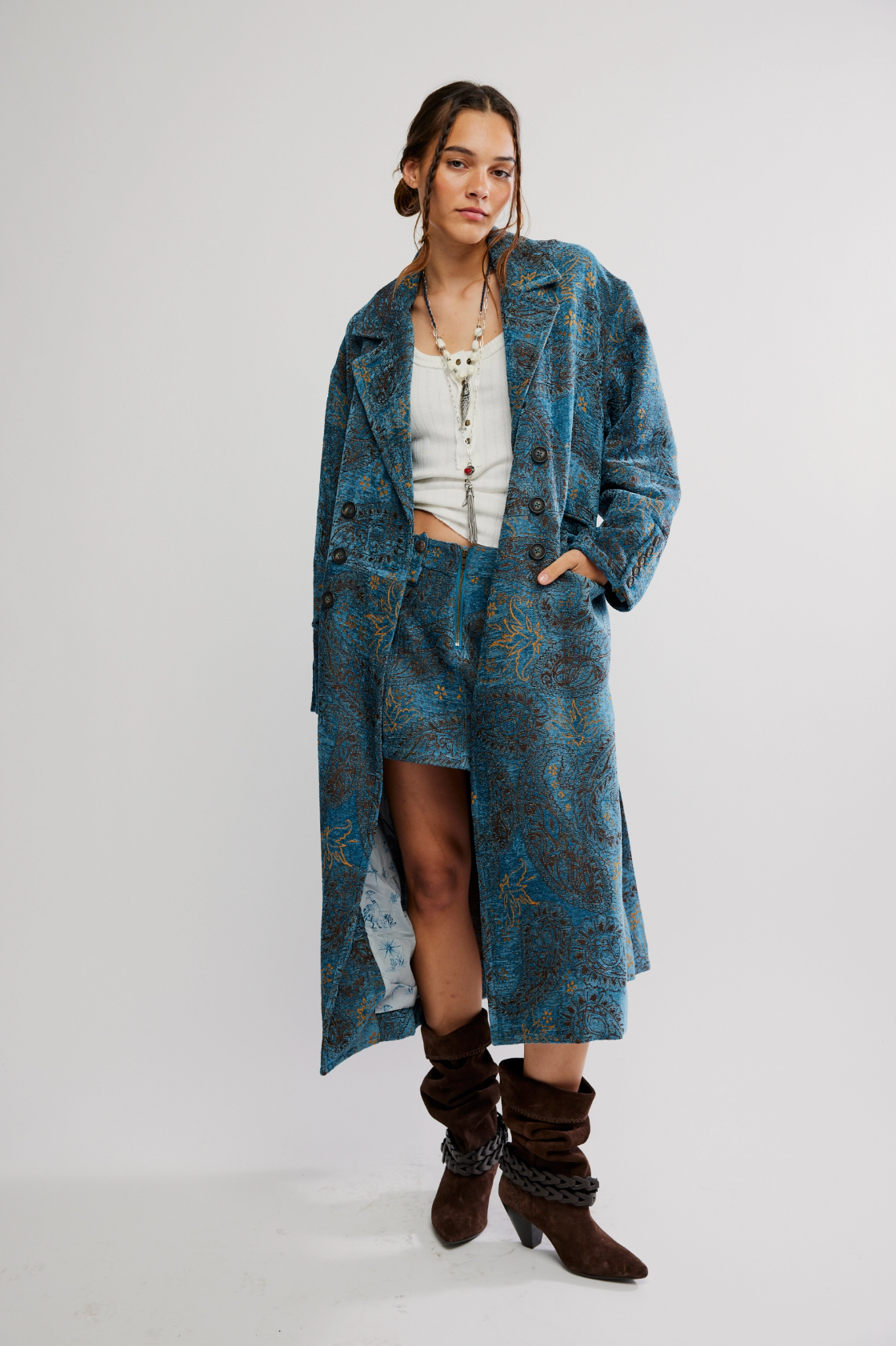 A woman models the Free People Micha Duster and matching skirt with a white top, layered necklaces, and brown slouchy boots against a plain white background.