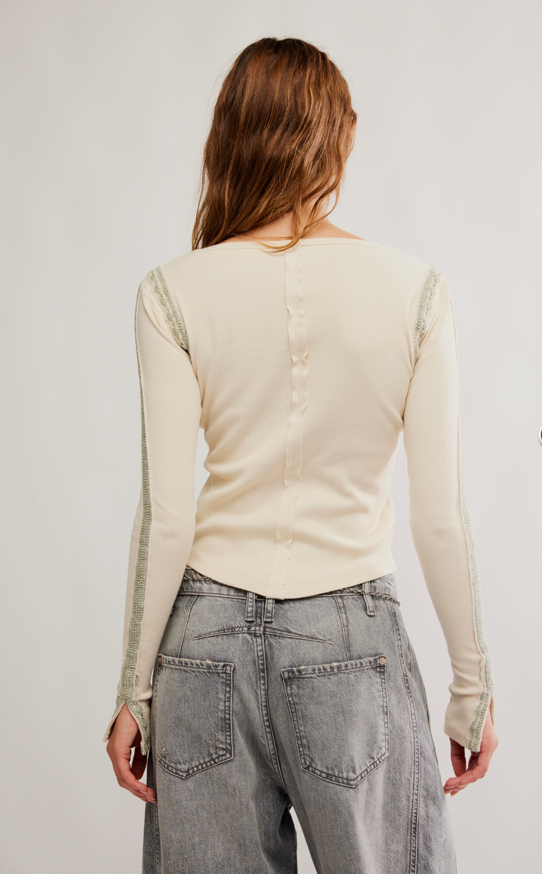 A person with long, wavy brown hair is shown from the back wearing Caravan’s Lost Love Long-Sleeve Top and gray high-waisted jeans with large back pockets.