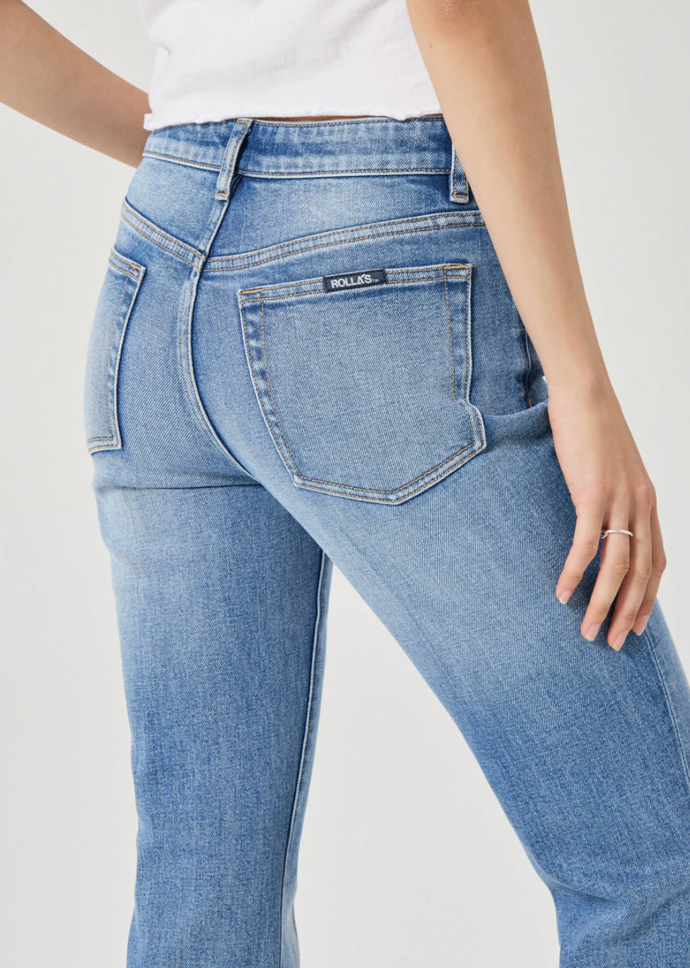 Close-up of a model wearing Rolla's Midtown Boot in Blue Iris jeans with a white top, showing back pockets and fit.