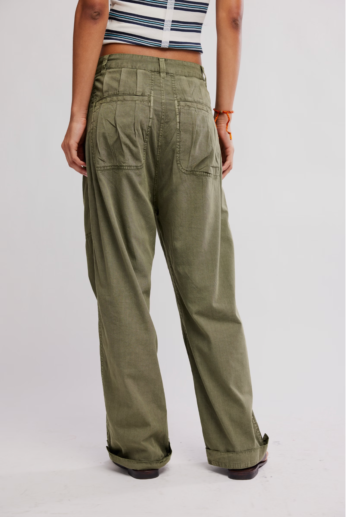 Back view of loose olive green Clover Dropped Trouser by Free People worn with a cropped striped top and cuffed hems.