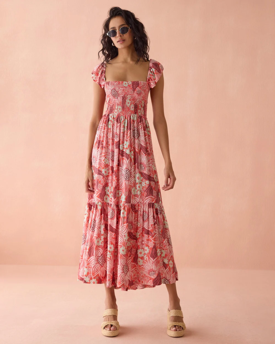 Woman wearing Zoe Maxi Dress by Omika with floral print and smocked bodice, styled with sunglasses and woven sandals.