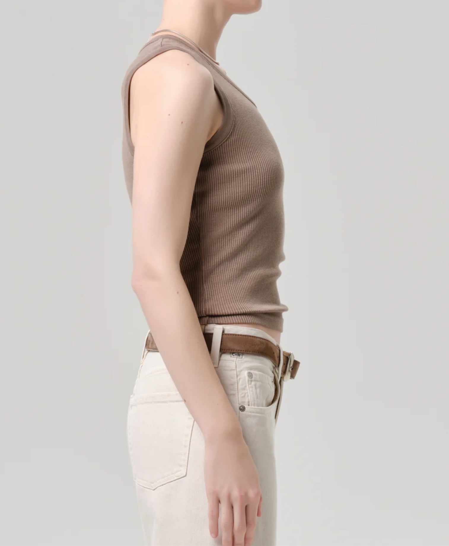 Side view of a model wearing The Nova Tank by Citizens of Humanity in Cocoa with white high-waisted pants and brown belt.