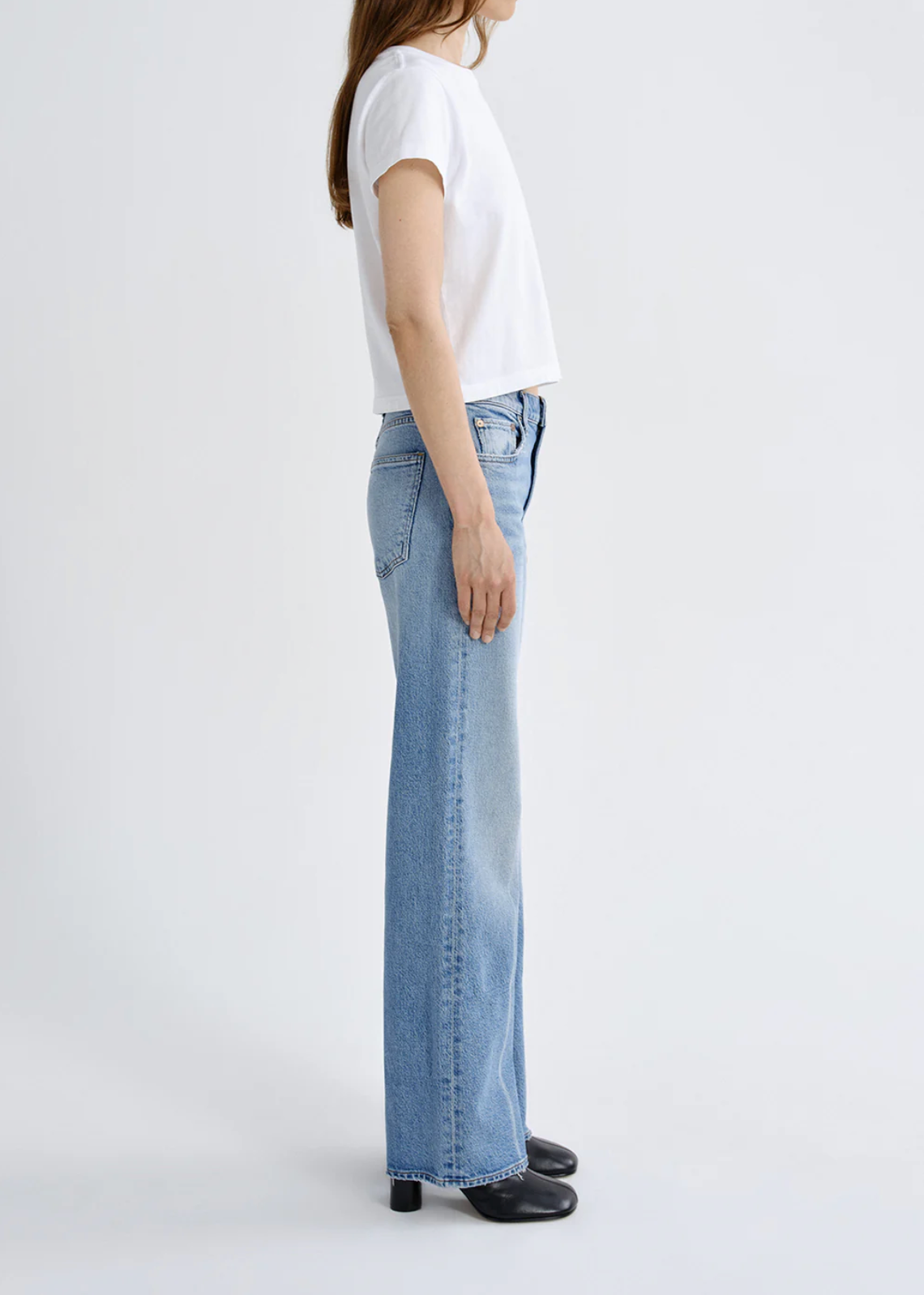 Side view of a woman wearing The Harper Jean in Outlook by Agolde with a white top and black shoes against a plain background