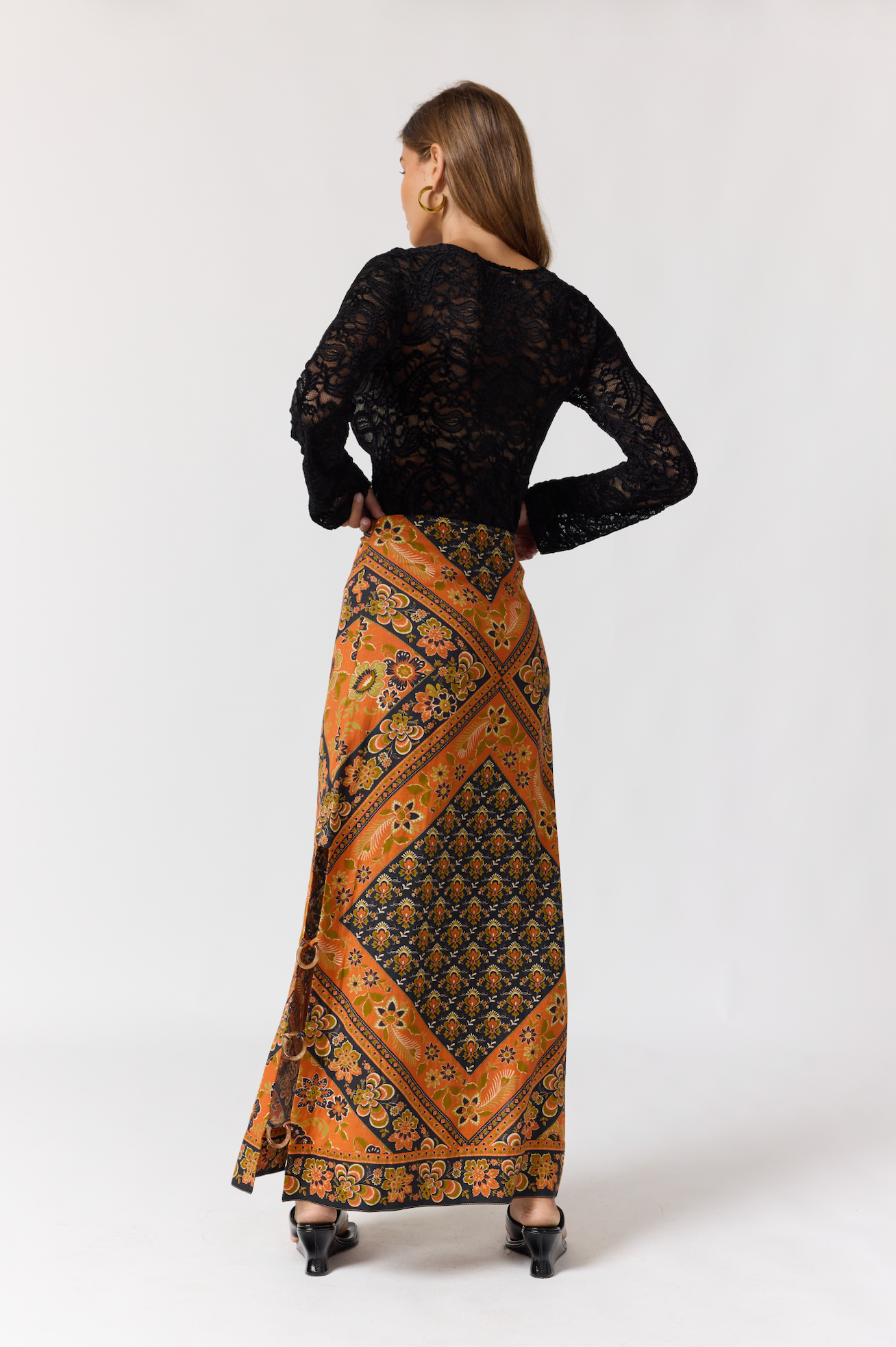 Woman wearing a patterned Whitney Skirt in Saffron paired with a black lace top and black heels posing back view.
