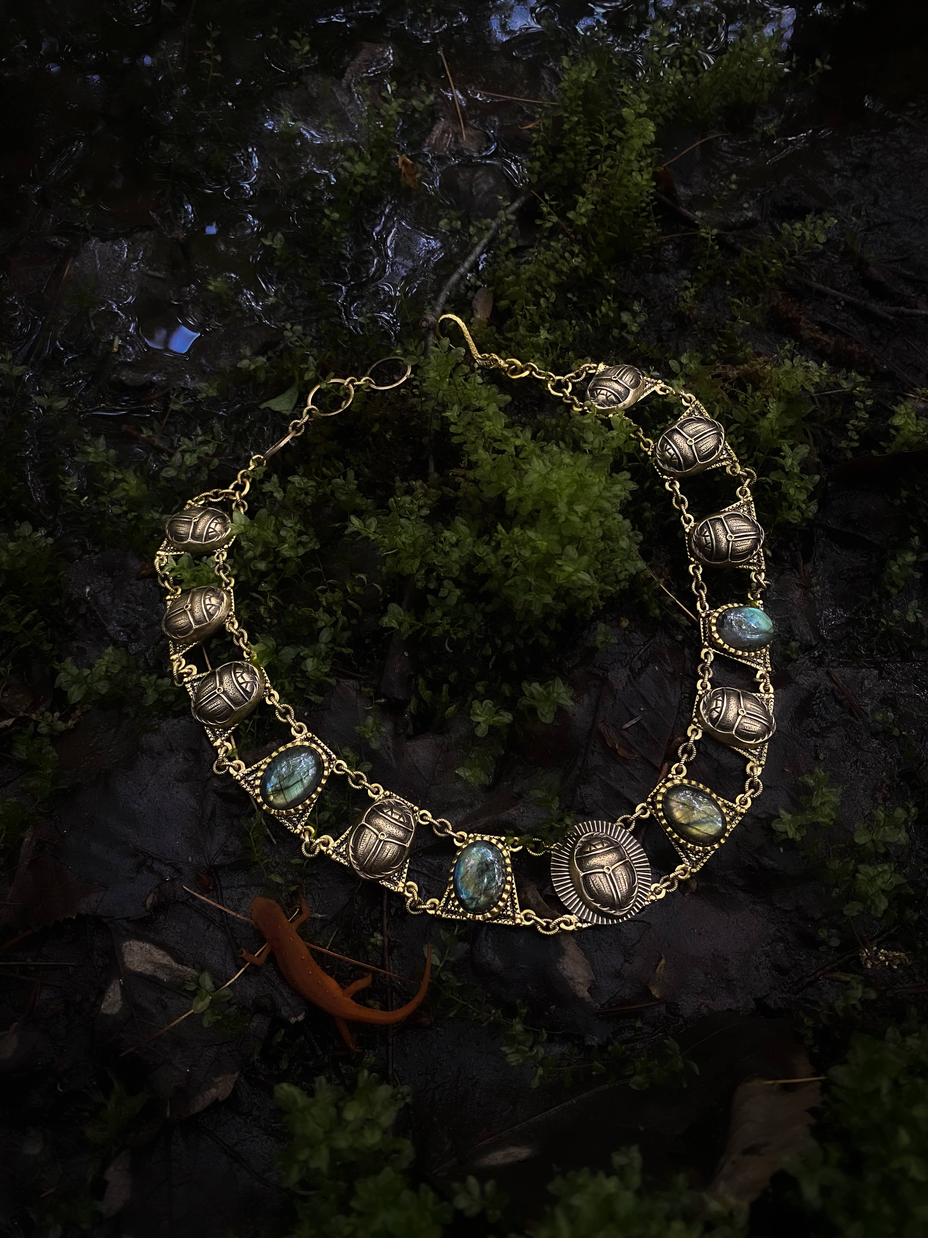 Sacred Scarab Collar Necklace with brass scarab charms and blue stone accents on natural moss background