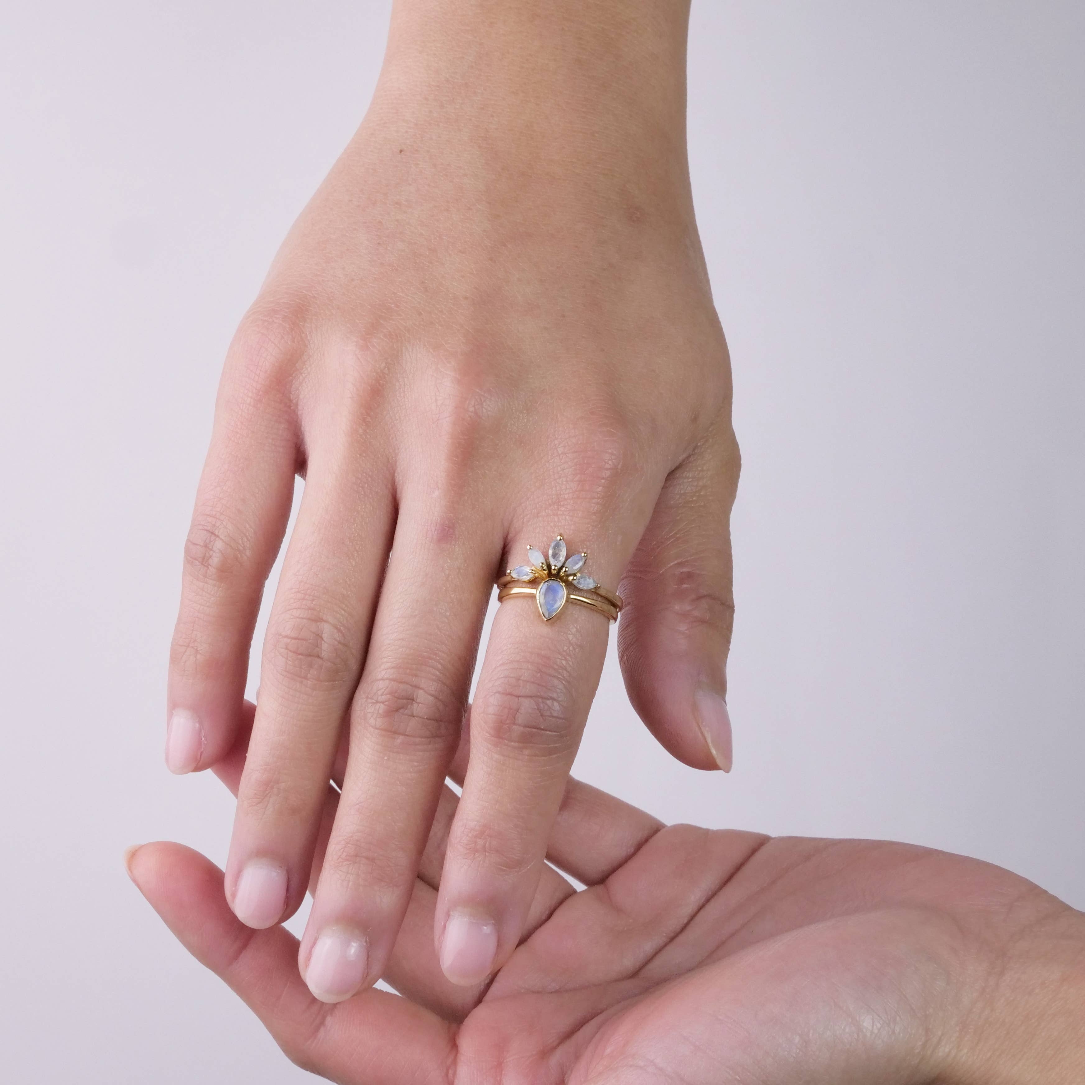 A close-up of one hand wearing the Baizaar Brass Nesting Moonstone Ring Set, featuring a light blue moonstone and small clear accents, gently resting on another open hand against a plain light background.