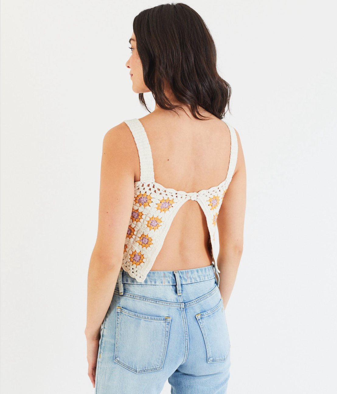 A woman with shoulder-length dark hair, wearing the Porter Blue Apparel REBEL STRAIGHT IN EDEN WASH jeans and a sunflower crochet crop top, stands facing away against a plain white background.