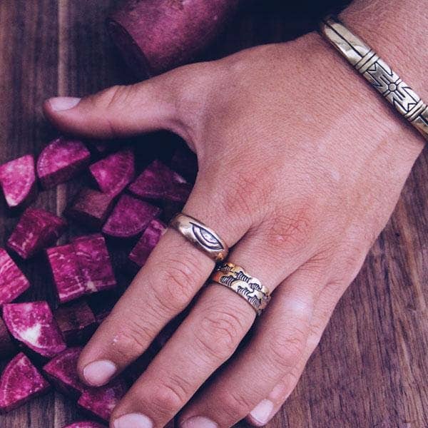 Hand wearing Medicine Wheel Cuff || Men silver bracelet and rings with carved designs over wooden surface with purple root vegetable pieces