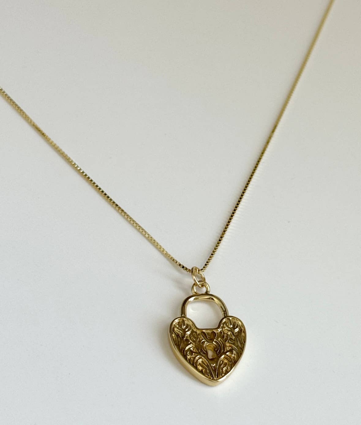 The Tramps+Thieves Since Ive Been Loving You Necklace, a gold vermeil piece with a heart-shaped pendant featuring intricate floral engravings, is displayed on a white background.