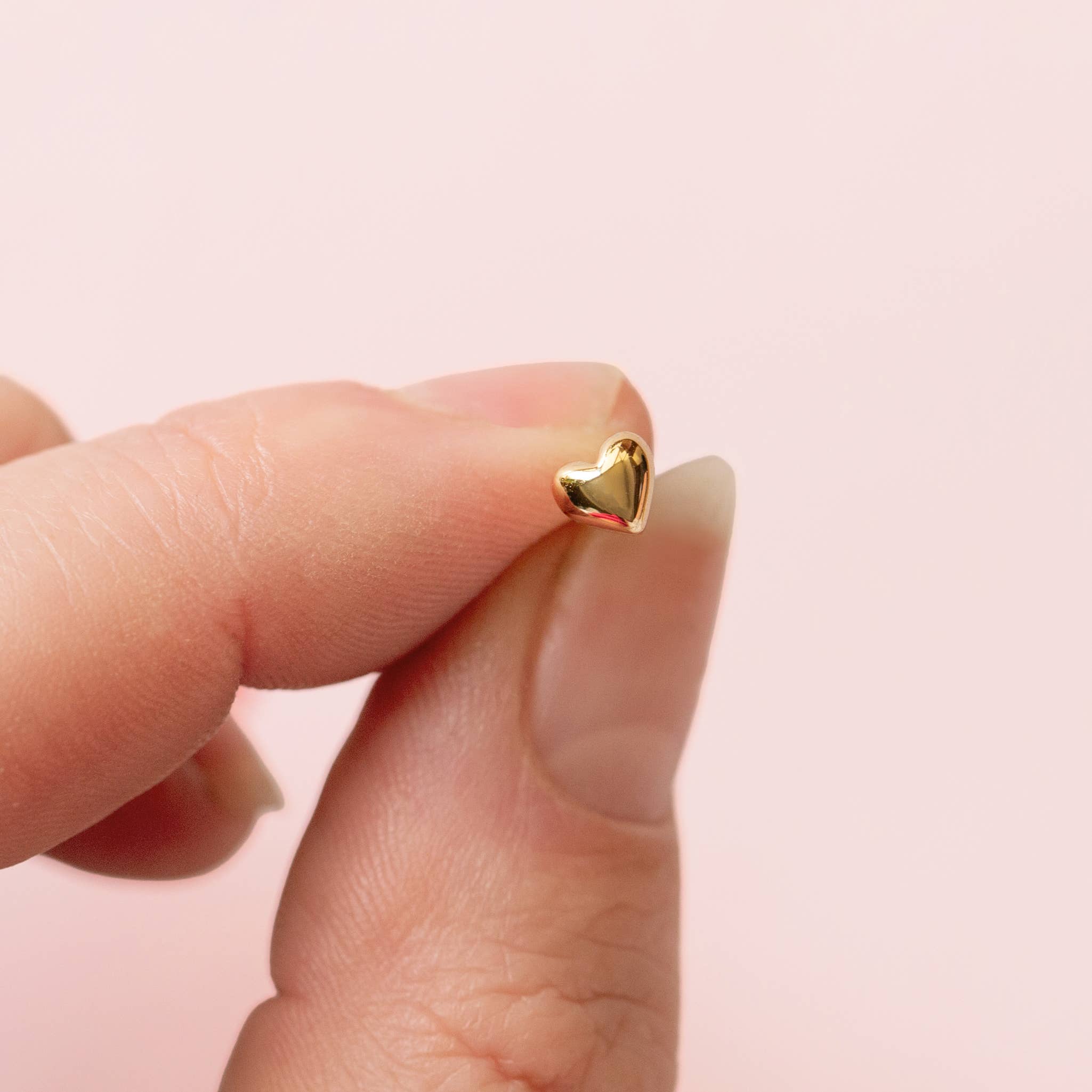 Small gold heart-shaped stud earring held between fingers, Bubble Heart Studs | Valentine's Day jewelry accessory