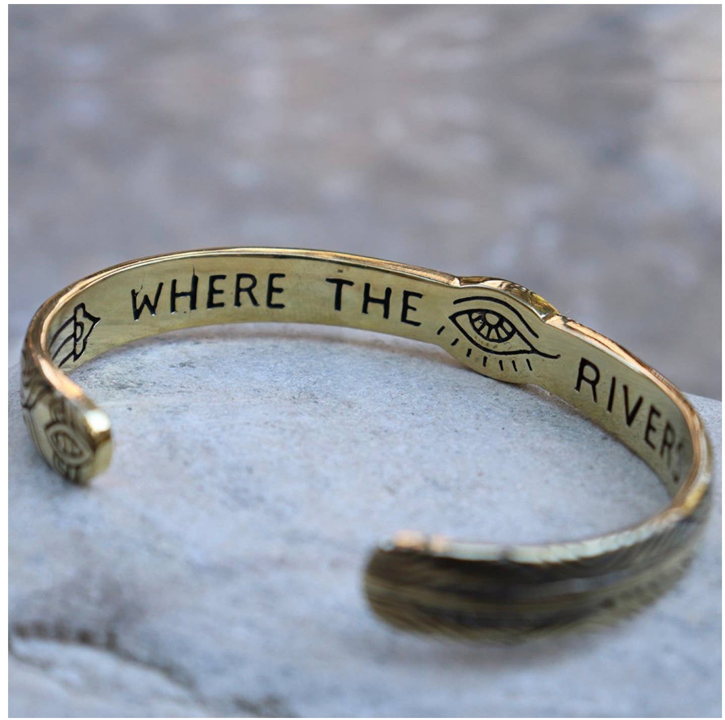Three Rivers Cuff brass bracelet with engraved eye and leaf designs and the phrase "Where the river" inside.