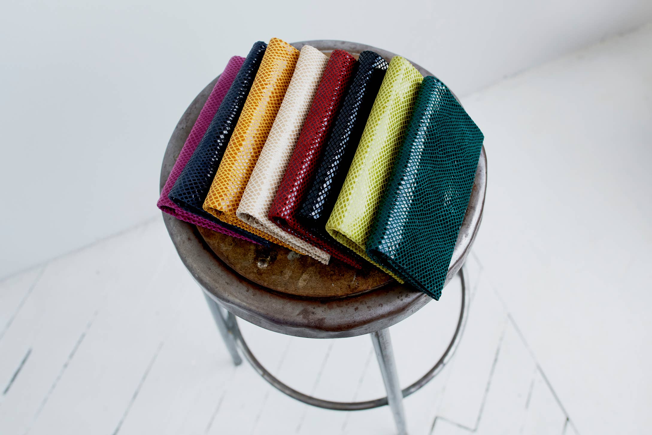 Gio Handcrafted Leather Wallet in various vibrant colors arranged on a rustic metal stool against a white background
