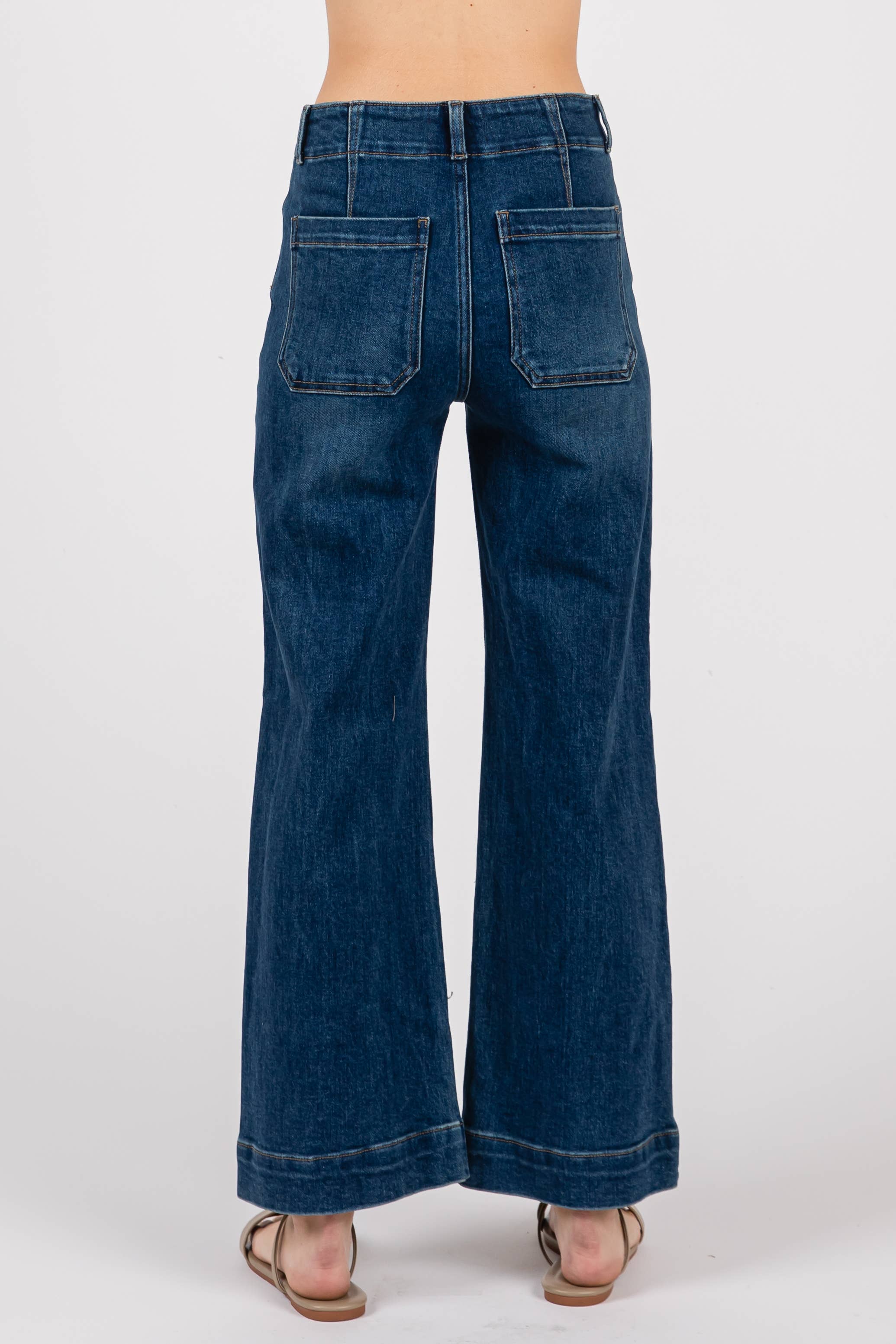 Someone wearing the L.T.J Letter to Juliet Dart Detail Wide Crop Jeans—high rise, wide-leg blue jeans with large back pockets—and tan sandals, shown from the waist down, photographed from behind against a plain white background.