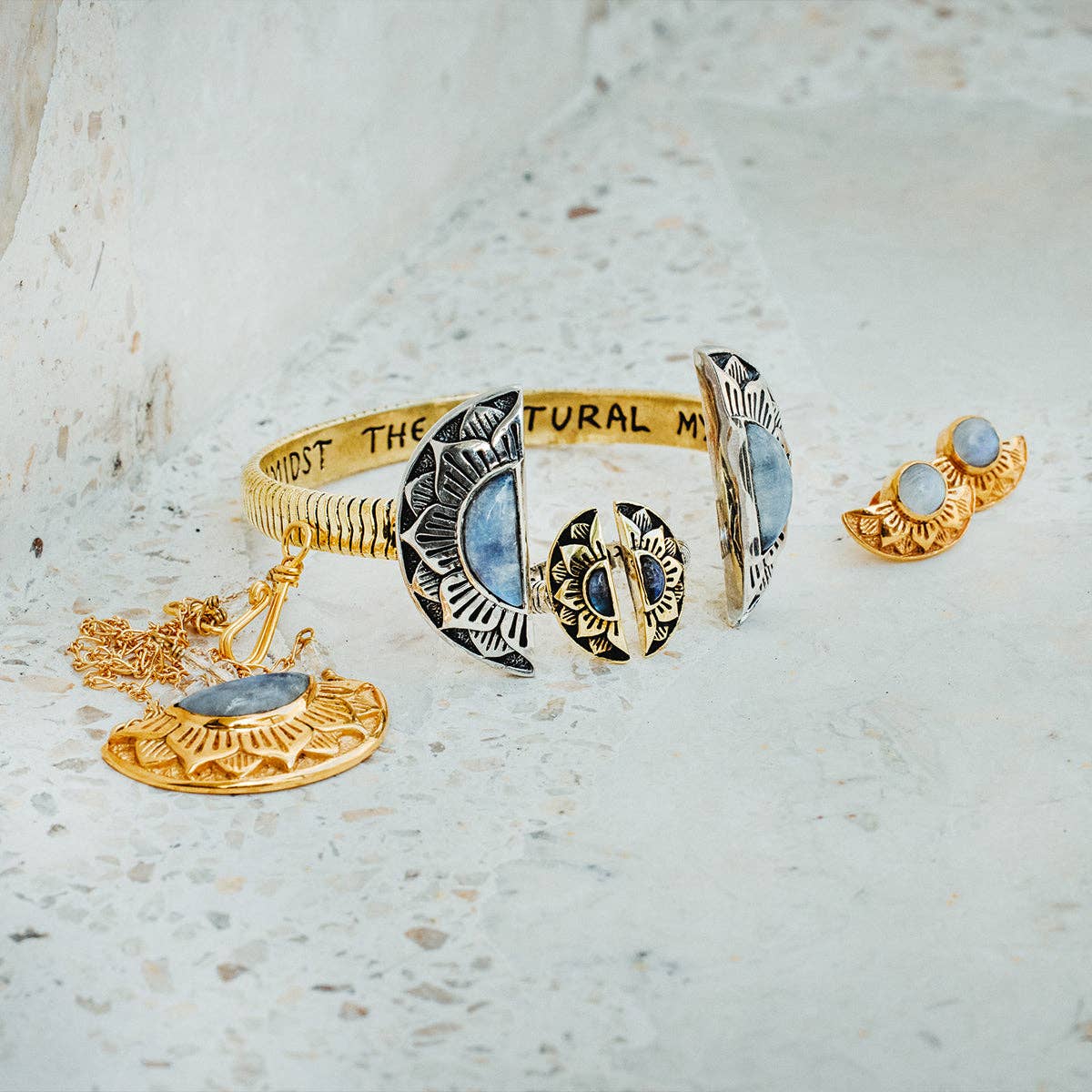 A set of gold and silver moon-themed jewelry with blue stones, including a bracelet, necklace, earrings, and the bahgsu jewels Natural Mystic Ring - Moonstone, styled as a talisman ring and displayed on a light, textured surface.
