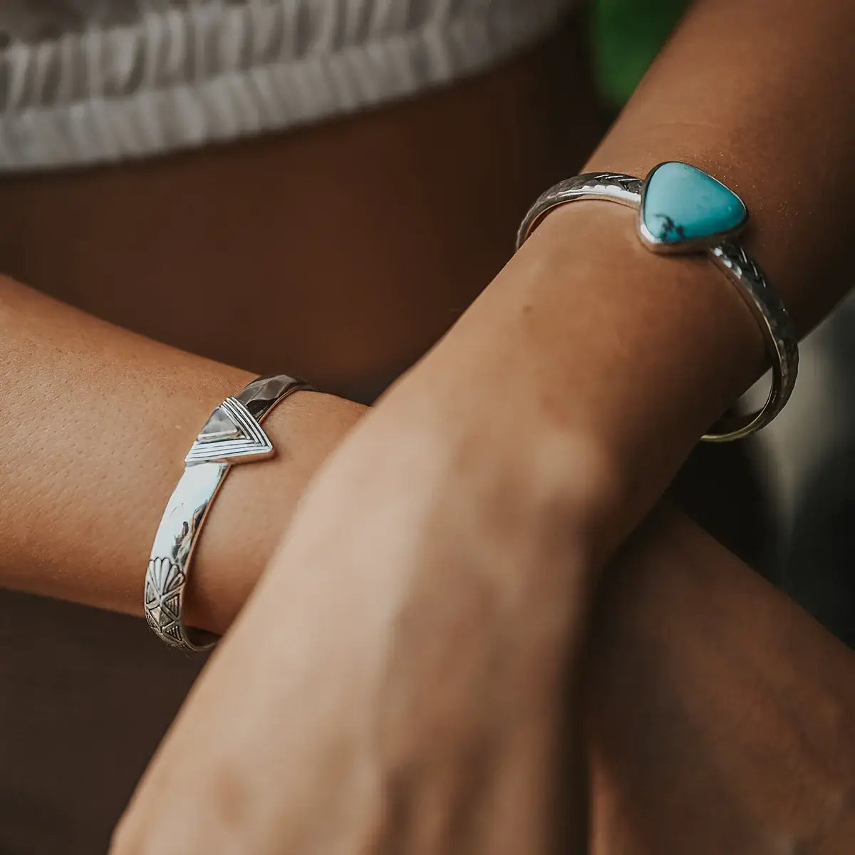 Close-up of two wrists adorned with artisan Hold Space Cuff bracelets featuring silver and turquoise designs