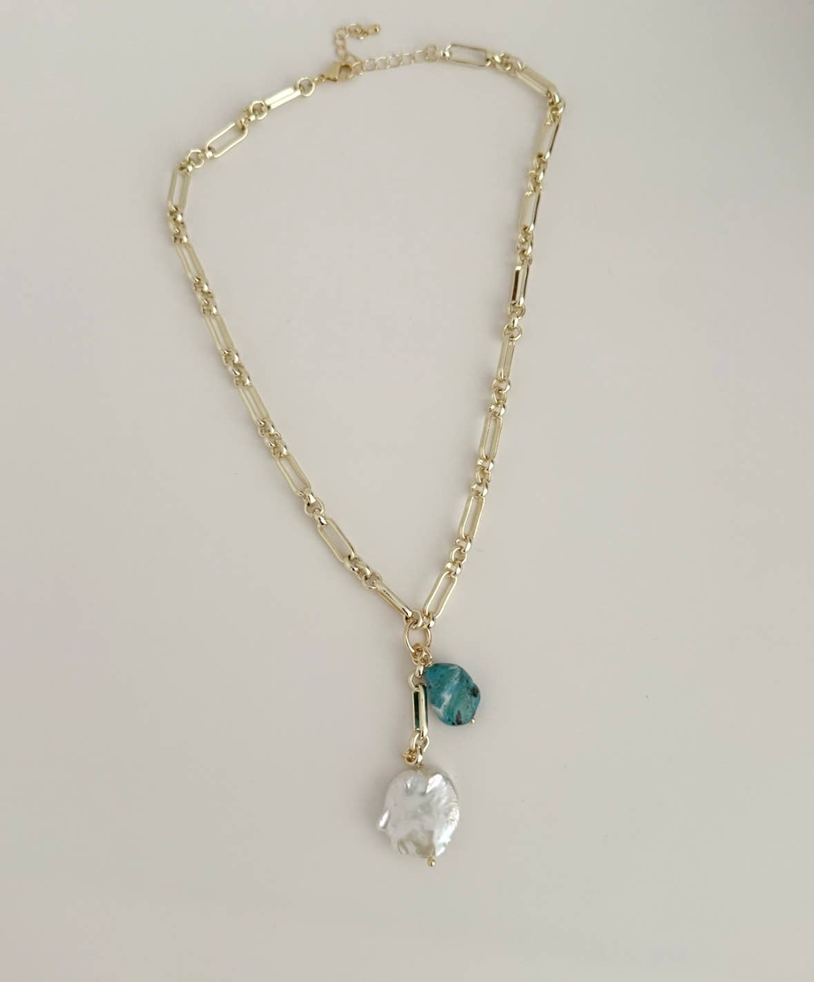 The Tramps+Thieves Azure Tide Necklace is an 18K gold-filled chain with a blue stone charm and a large white baroque pearl pendant, shown on a white background.