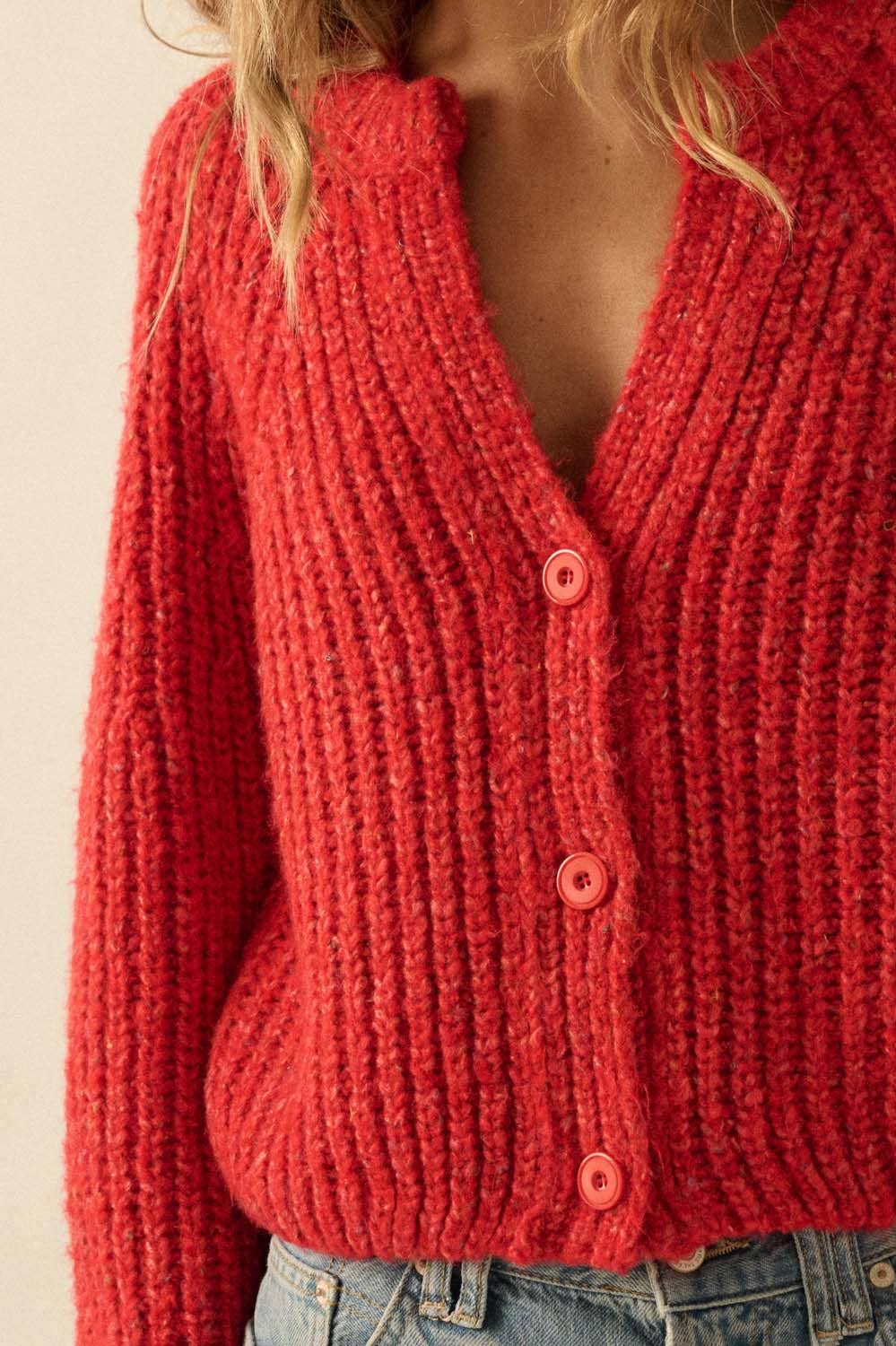A person wears the Promesa USA Confetti Button-Front Cardigan Sweater—a chunky, red, ribbed knit with three buttons and a deep V-neck—paired with blue jeans. The persons face is not visible.