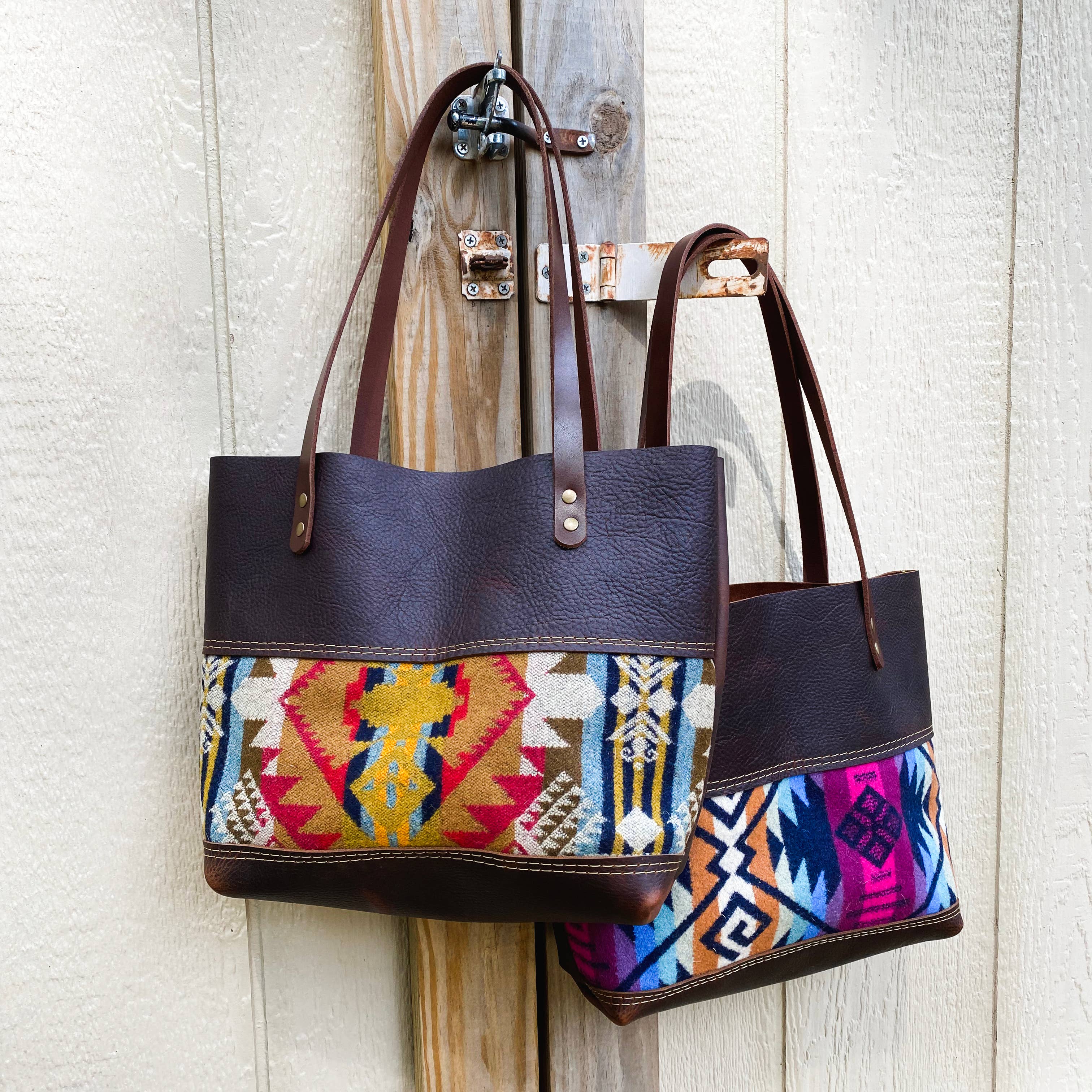 Two Hawks & Doves Wool Tote Short bags with geometric Southwestern-style Pendleton wool panels and brown full grain leather handles hang on a wooden post against a textured light wall.