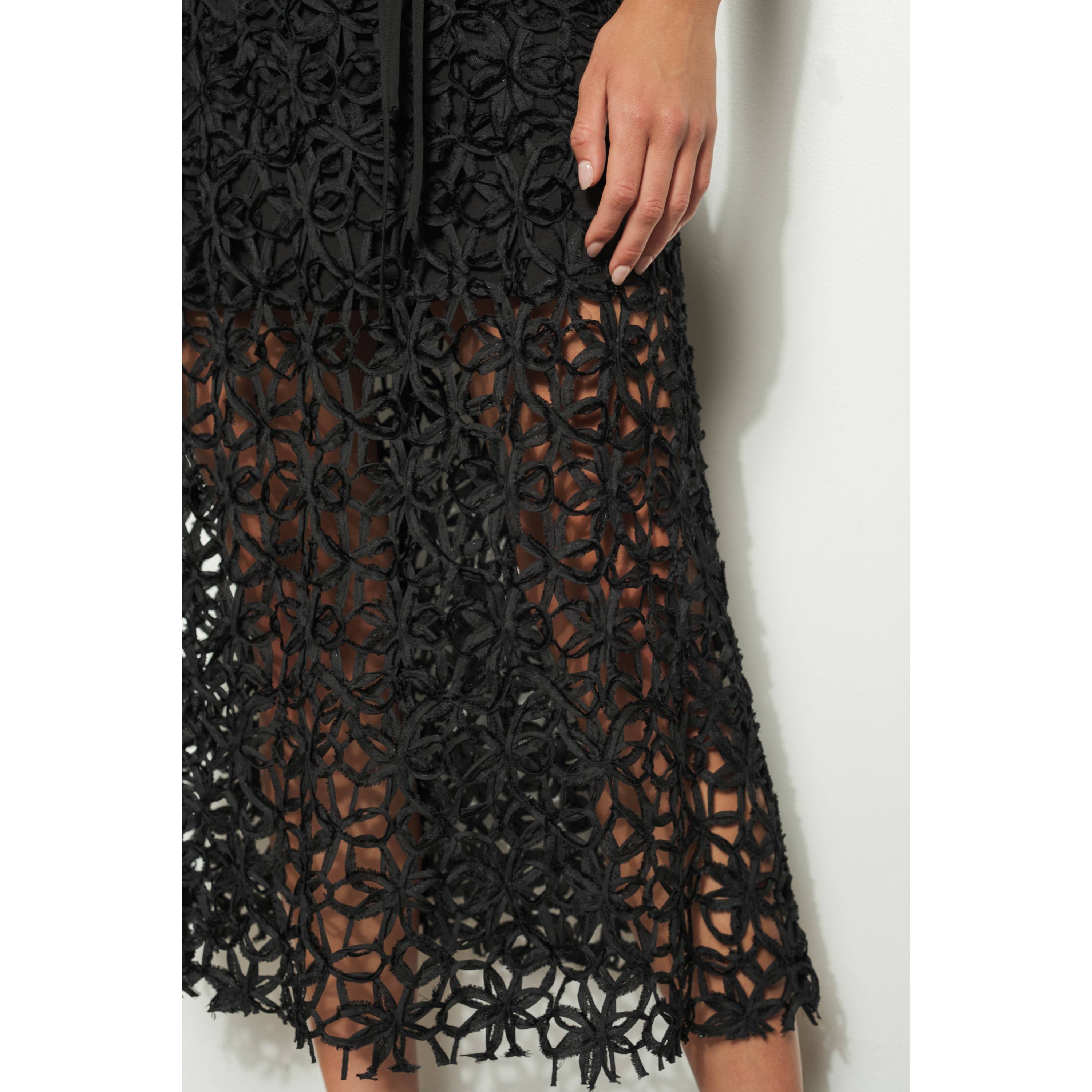 A close-up of a womans hand on her hip, wearing the INA Sleeveless Crochet Lace Overlay Midi Dress. The black semi-sheer crochet lace reveals her legs beneath, lending an elegant touch to the look.