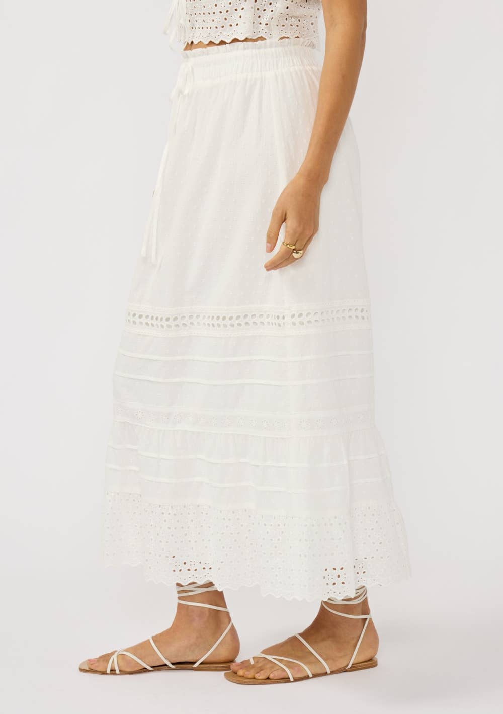 Woman wearing a white Eyelet Hem Pintuck Skirt with delicate eyelet details and soft pintuck layering, styled with sandals.