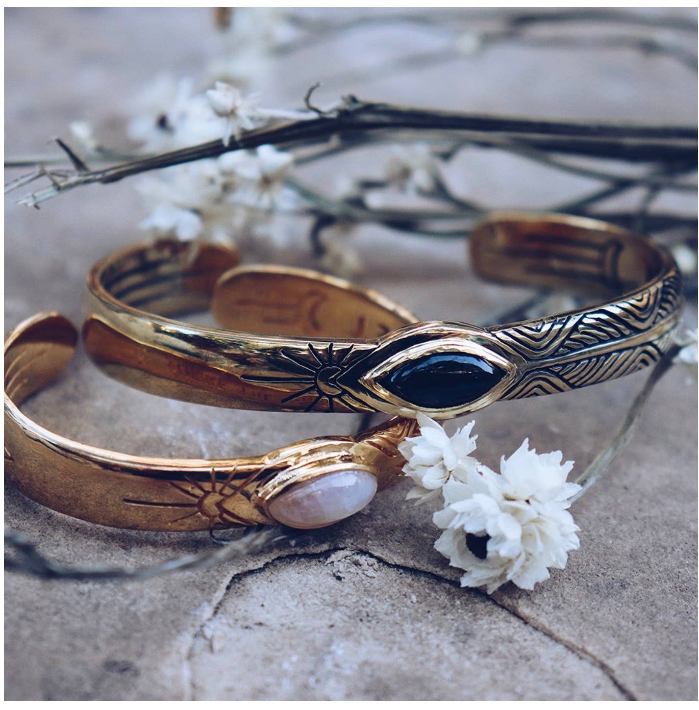 Close-up of two Three Rivers Cuff bracelets with intricate designs, featuring black and white stones on a textured surface.
