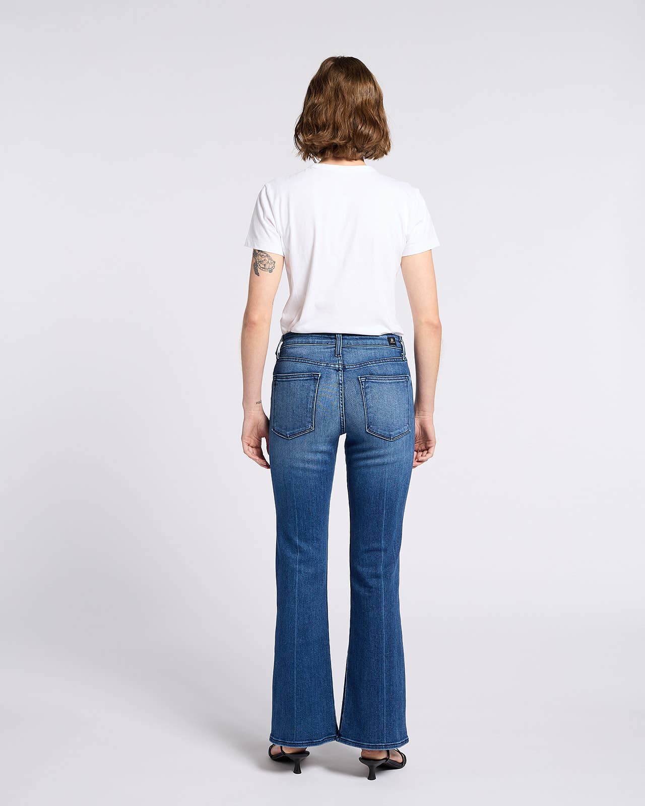 Woman wearing Bella Whisker Flare Denim jeans, shown from the back with a white t-shirt and black heels.