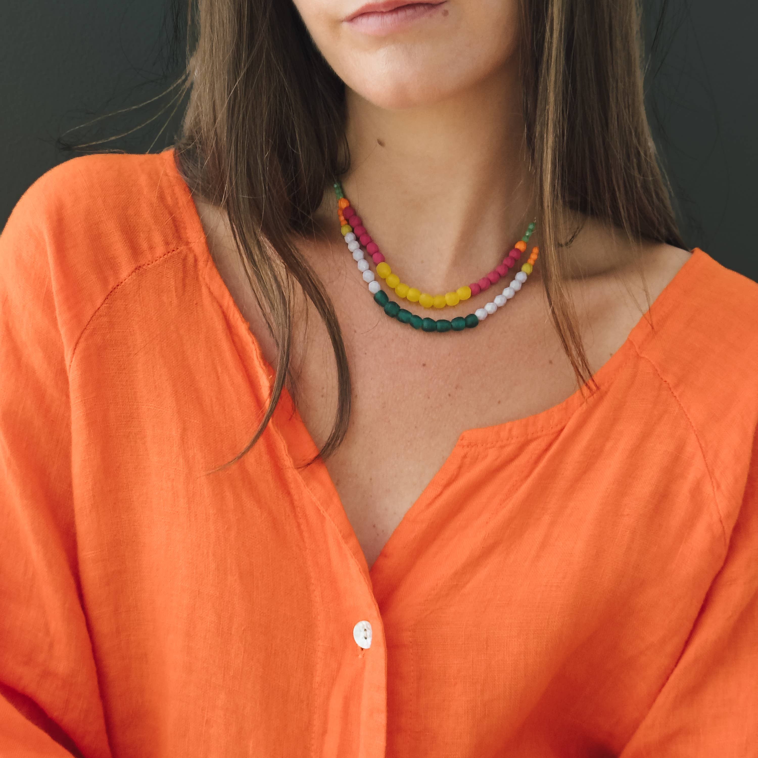 Close-up of woman wearing Multicolor Recycled African Glass And Mixed Bead Necklace with vibrant beads and casual orange top