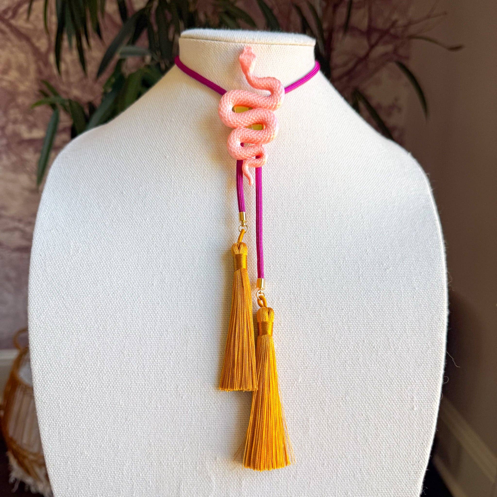 Snake Bolo Sugar Pink with Fuchsia & Golden Yellow necklace featuring a coiled snake and tassel accents on a display bust