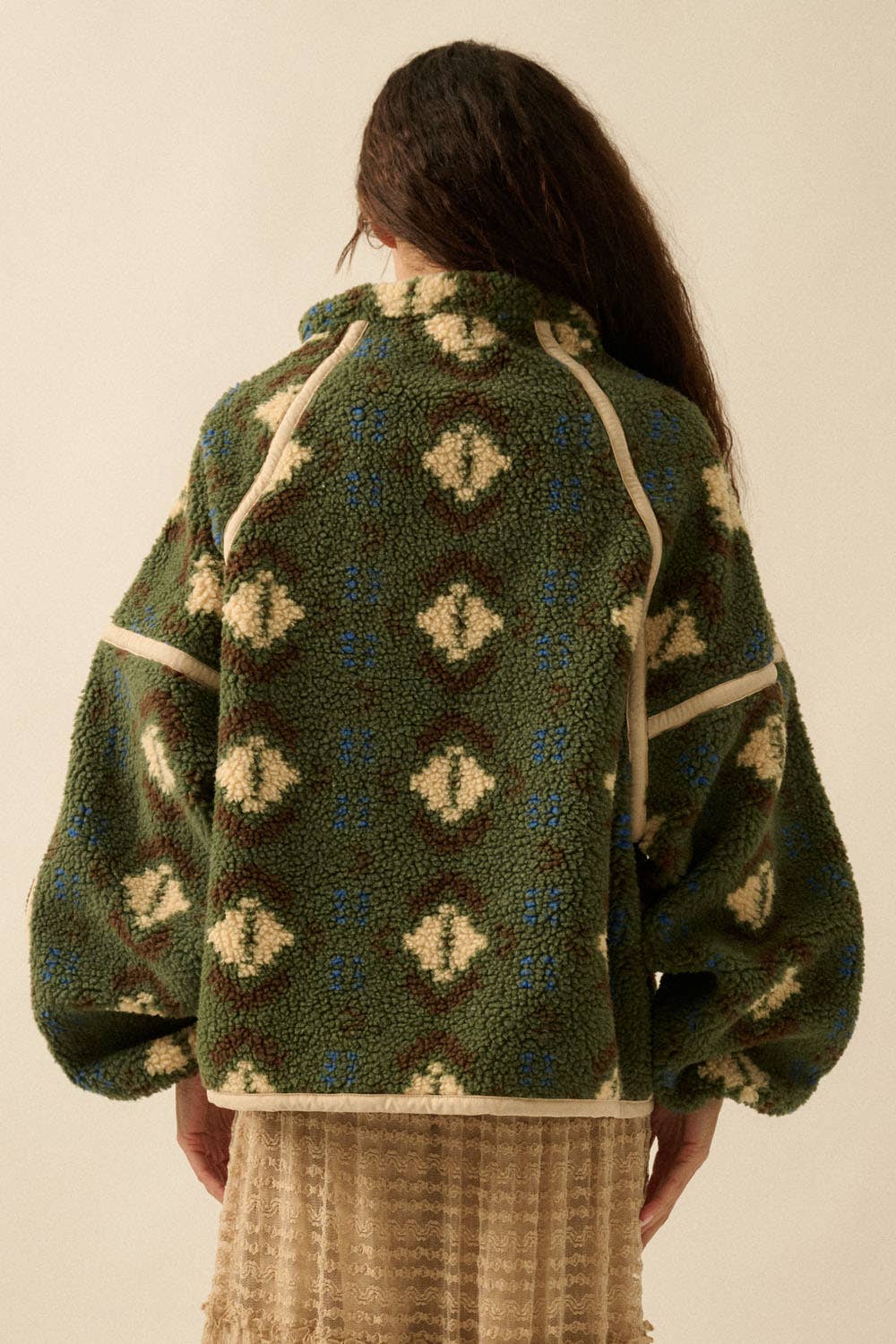 A person with long brown hair faces away, wearing the Promesa USA Geo-Print Sherpa Fleece Half-Zip Pullover Jacket with puffy sleeves and a high collar, paired with a beige textured skirt.