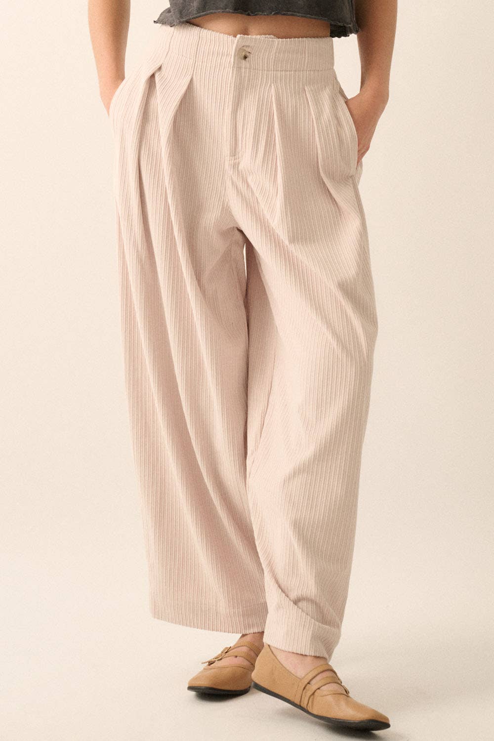 A person wears Promesa USA Velvet Corduroy Pleat-Front Wide-Leg Pants in light beige with vertical stripes and a relaxed fit, paired with a grey top and tan flats. Only the lower half of their body is visible, hands tucked in their pockets.