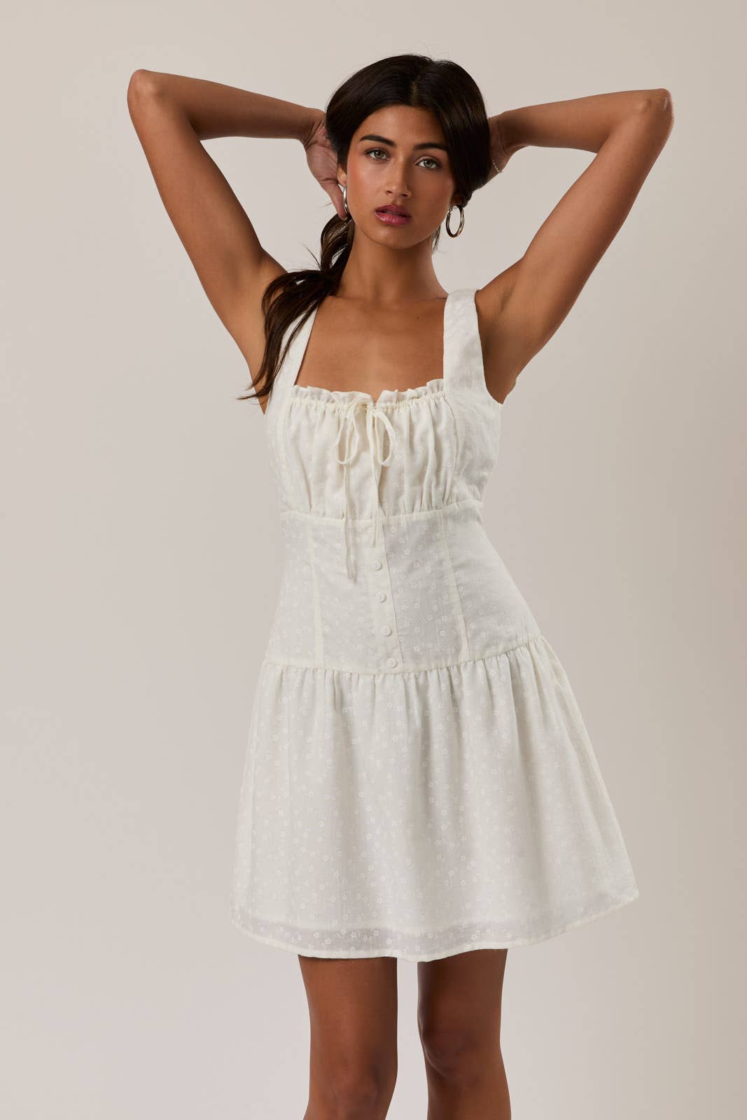 Woman wearing a white Shirred Neck Low Waist Mini Dress with wide straps and textured fabric, posing with arms raised.