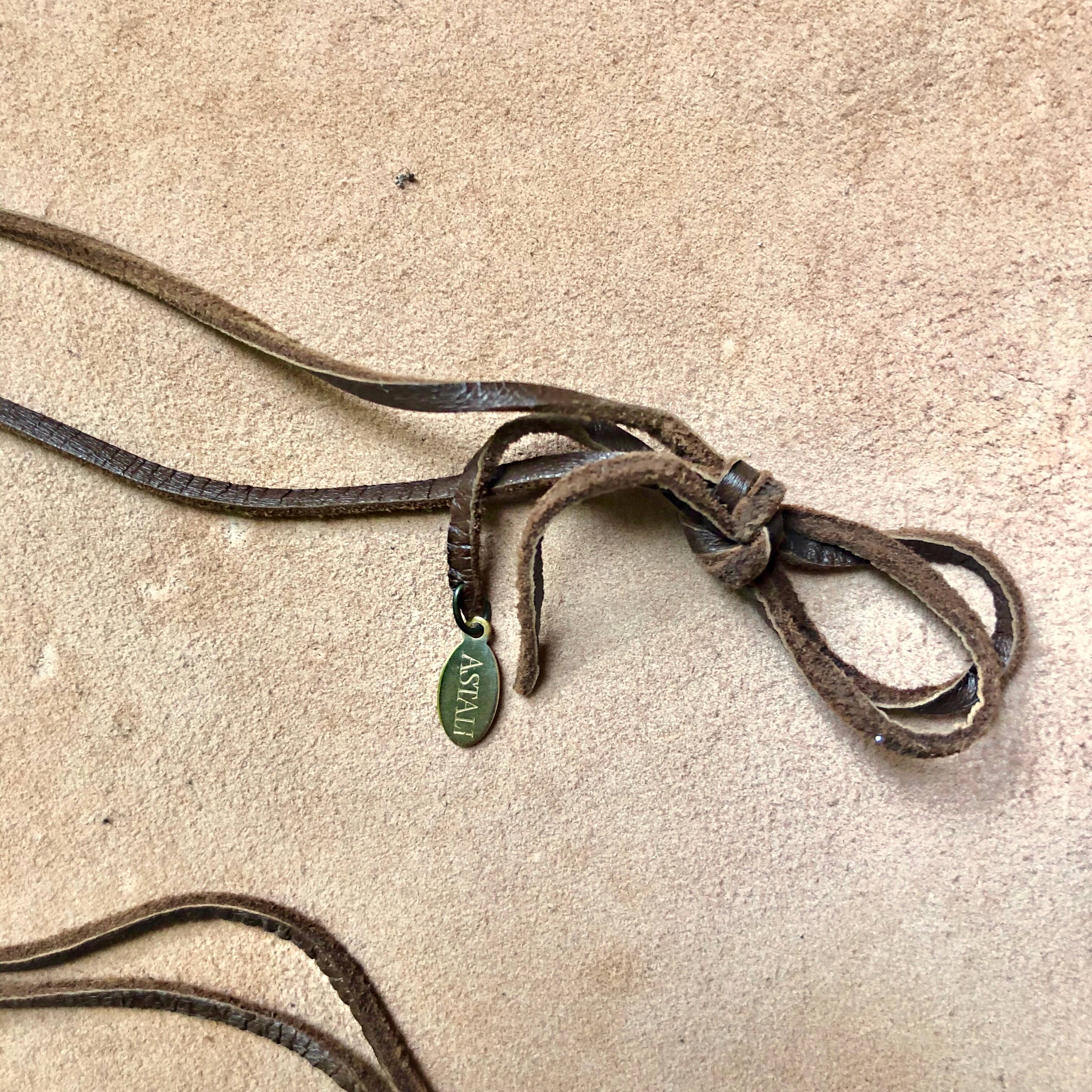 The ASTALI Vintage Pocket Knife & Coyote Tooth Necklace features pyrite and deerskin leather, with a small gold MKSY tag, displayed on a tan textured surface.