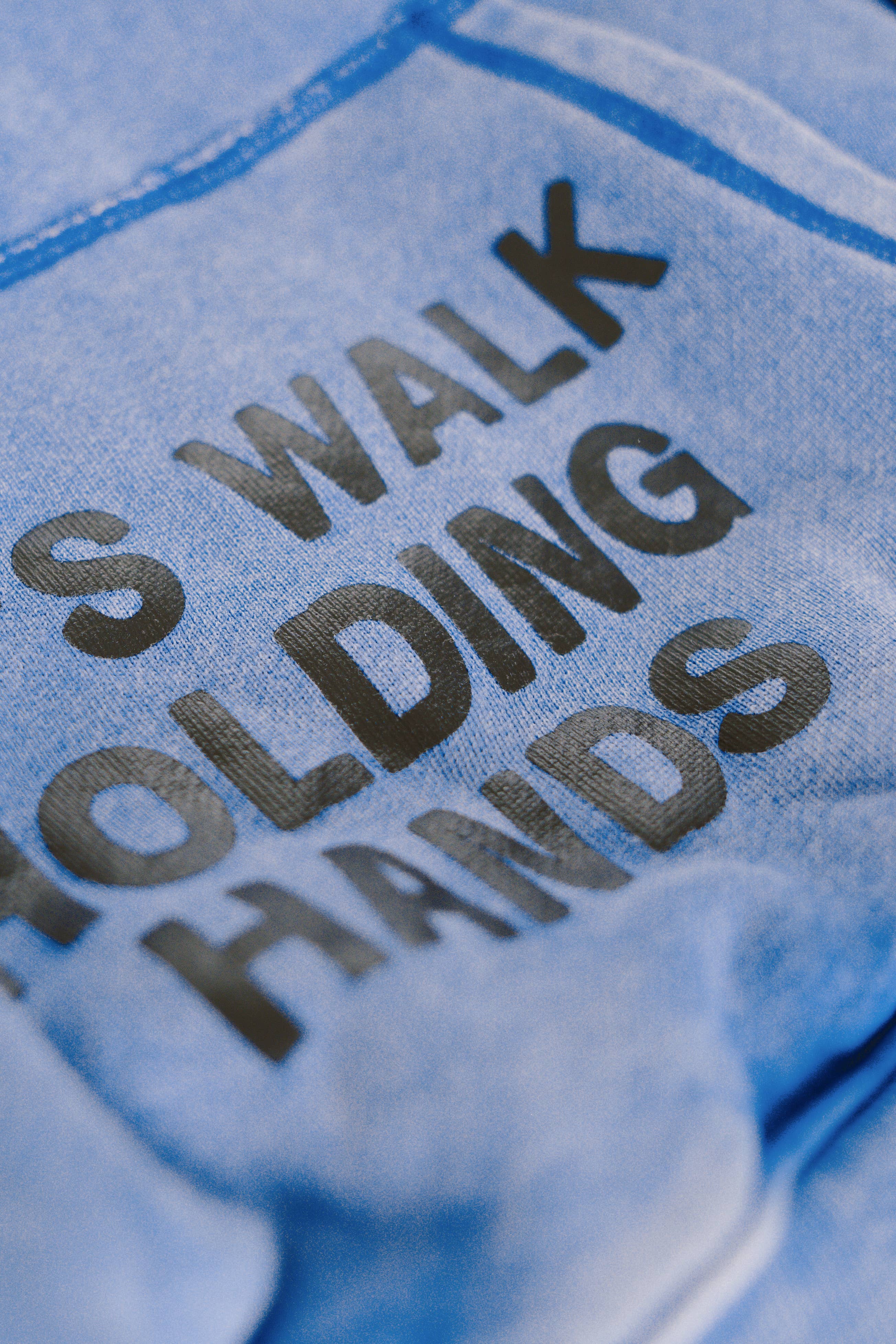 Close-up of blue fabric with bold black text reading "S WALK HOLDING HANDS" on the SORRY MOM HOODIE - PRESALE