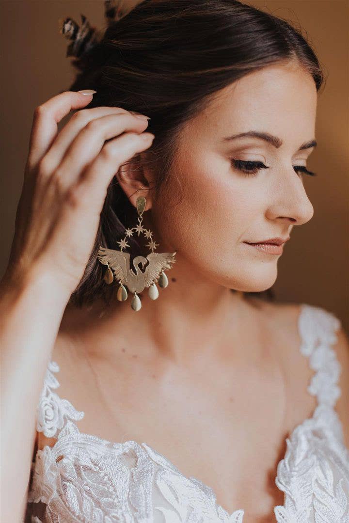 Celestial Swans earrings worn by a woman in a white lace dress with celestial star details