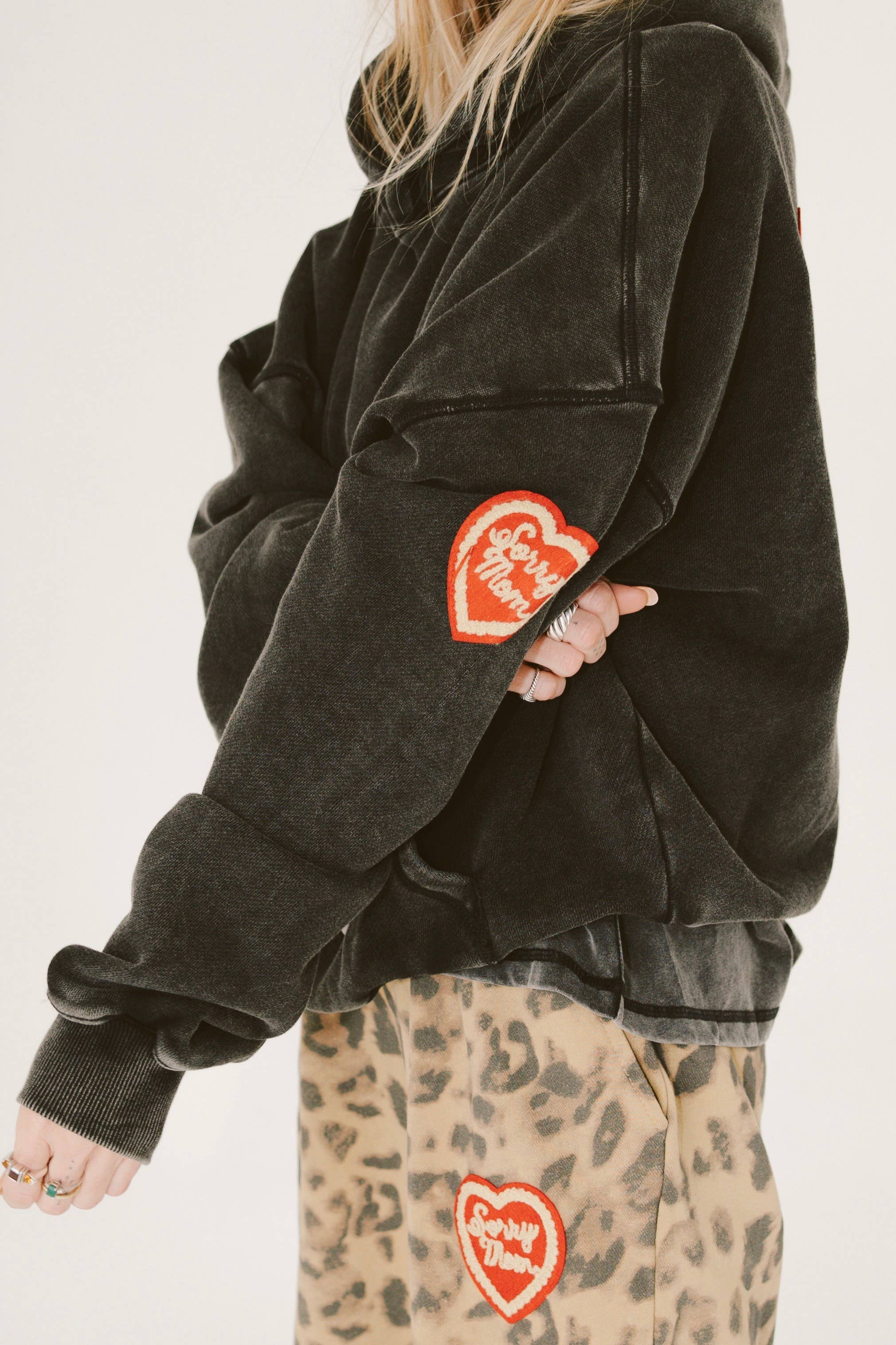 Person wearing black SORRY MOM HOODIE - PRESALE with heart patch and leopard print pants with matching patch