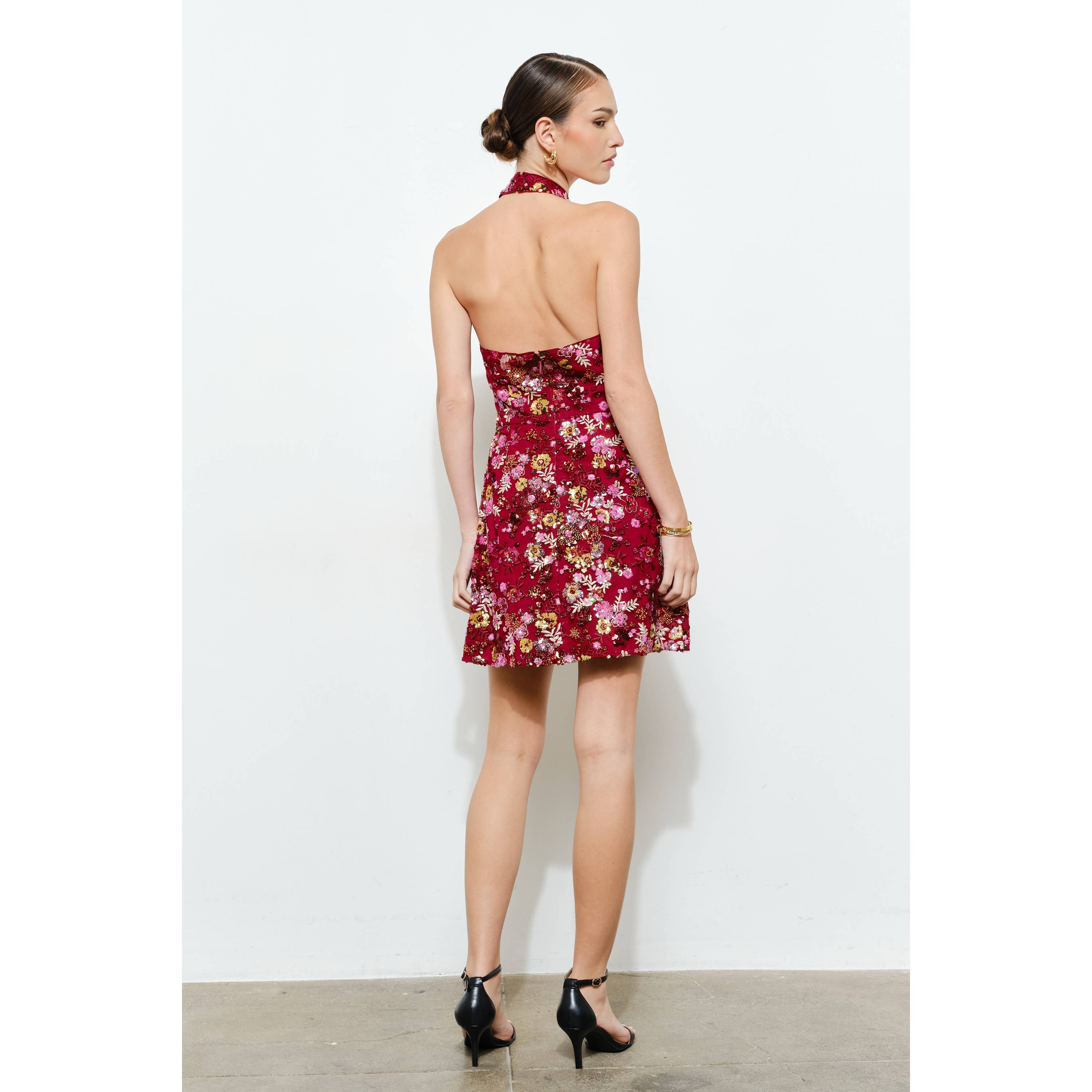 Woman wearing a backless Floral Sequins Embellished Halter Neck Mini Dress in rich red with floral patterns and black heels